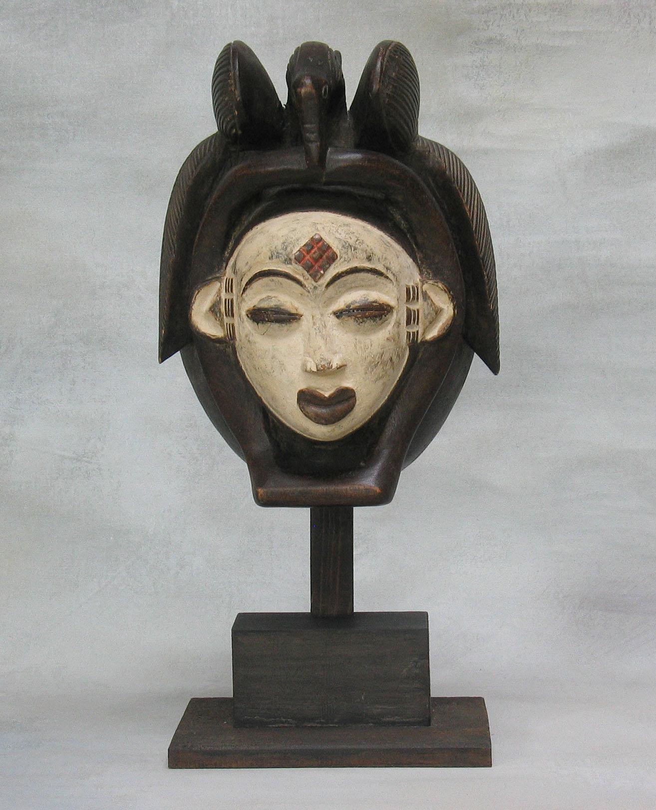 A Punu mask
Gabon, 20th century,
Of classical form, the white-faced mask 
with high double crested coif and side braids, 
raised scarification between the eyes and at the temples. 
finely delineated eyebrows, pursed lips.
On custom wood