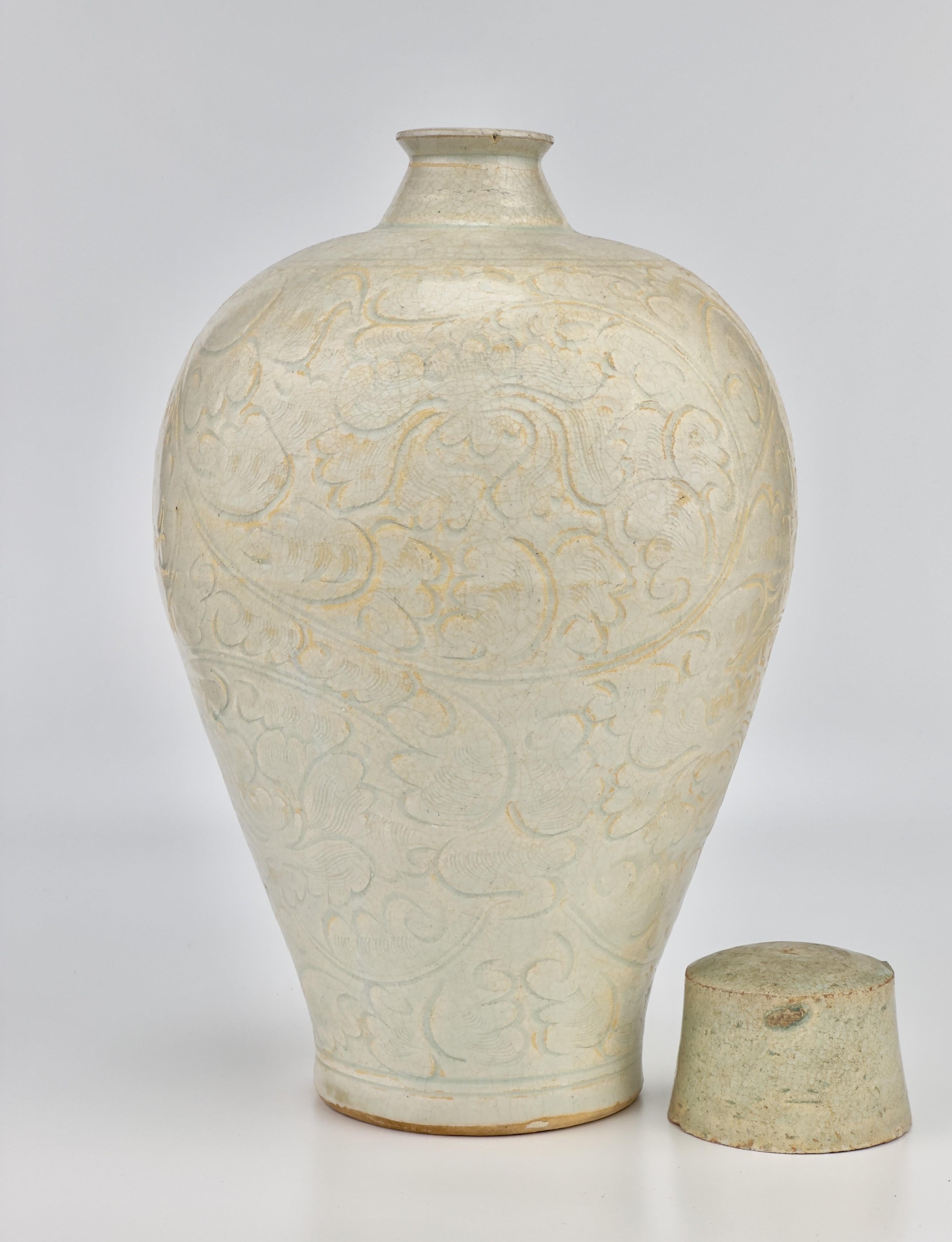 The vase exhibits a finely crafted structure, characterized by its wide shoulders and elongated, tapering sides, topped with a compact, ribbed cylindrical neck. Its exterior is adorned with intricately carved scrolling foliage motifs, accentuated by