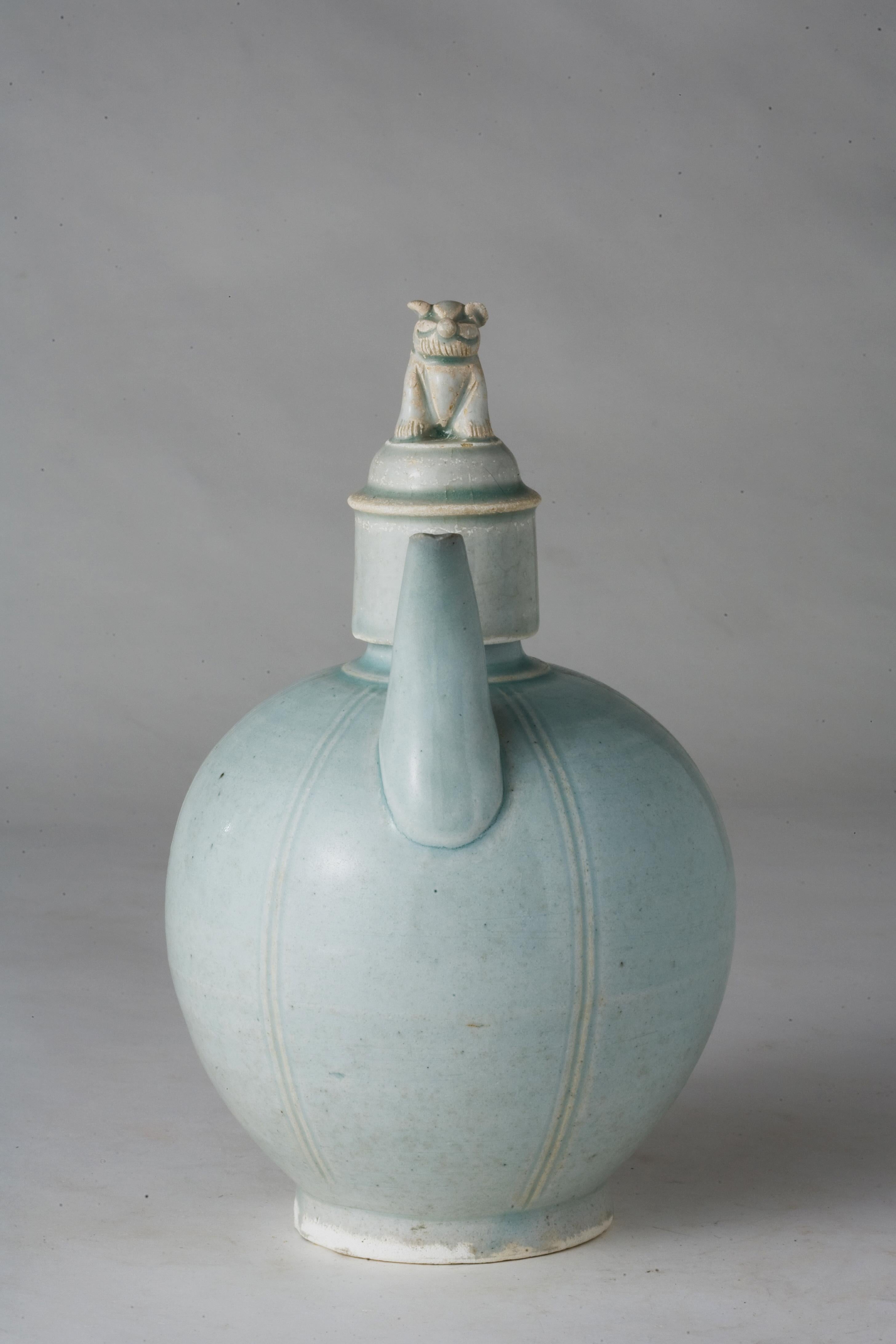 L'aiguière présente un corps globulaire avec un bec droit et une poignée arquée, créant une impression de stabilité équilibrée. Quatre lignes verticales incisées courent régulièrement le long du corps, soulageant la surface de la monotonie tout en