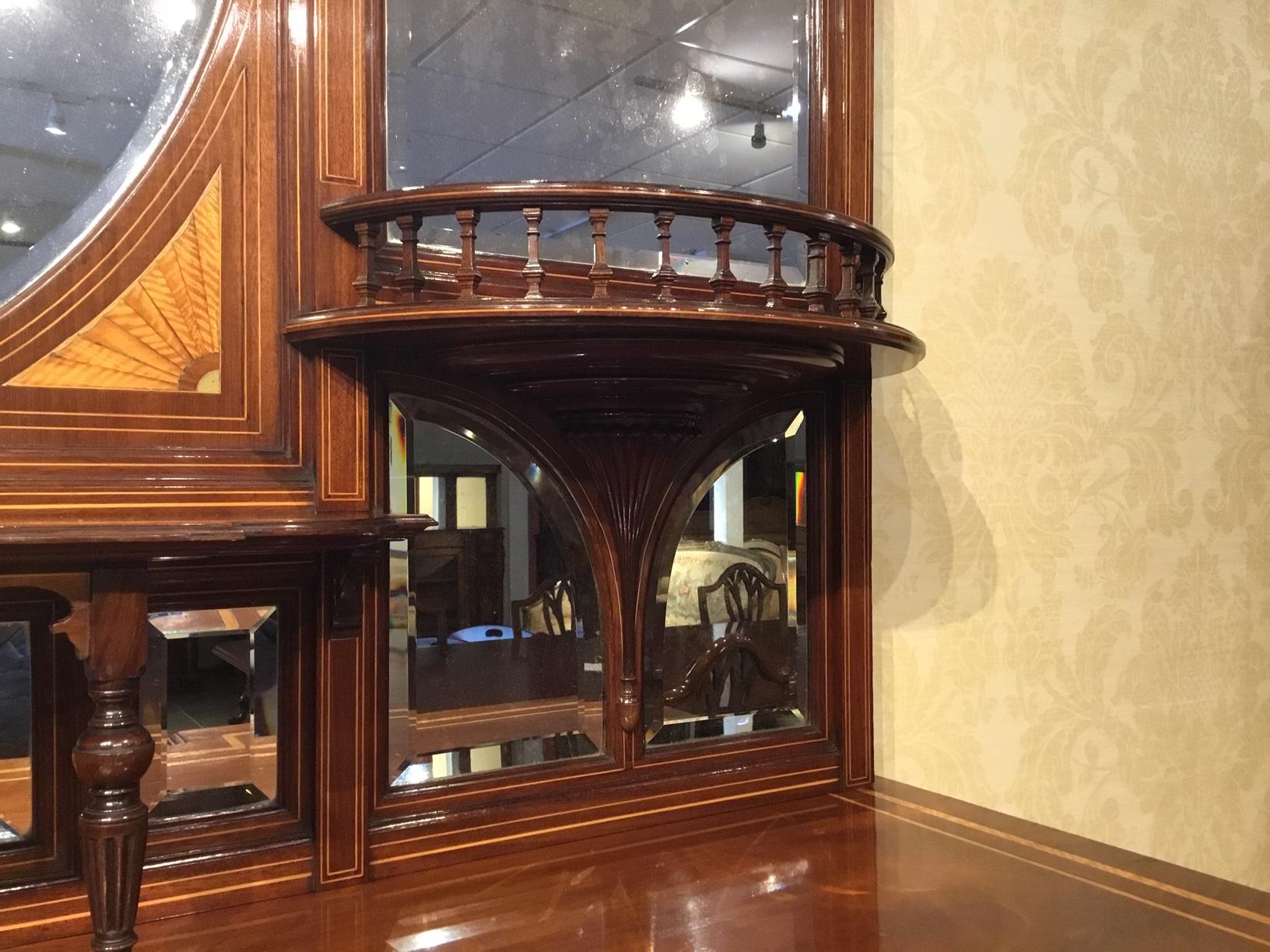 A quality mahogany inlaid late Victorian period chiffonier. The upper section having an architectural pediment centred by a turned finial with Sheraton style inlaid detail. The mirrored back has a central oval bevelled mirror again with Sheraton