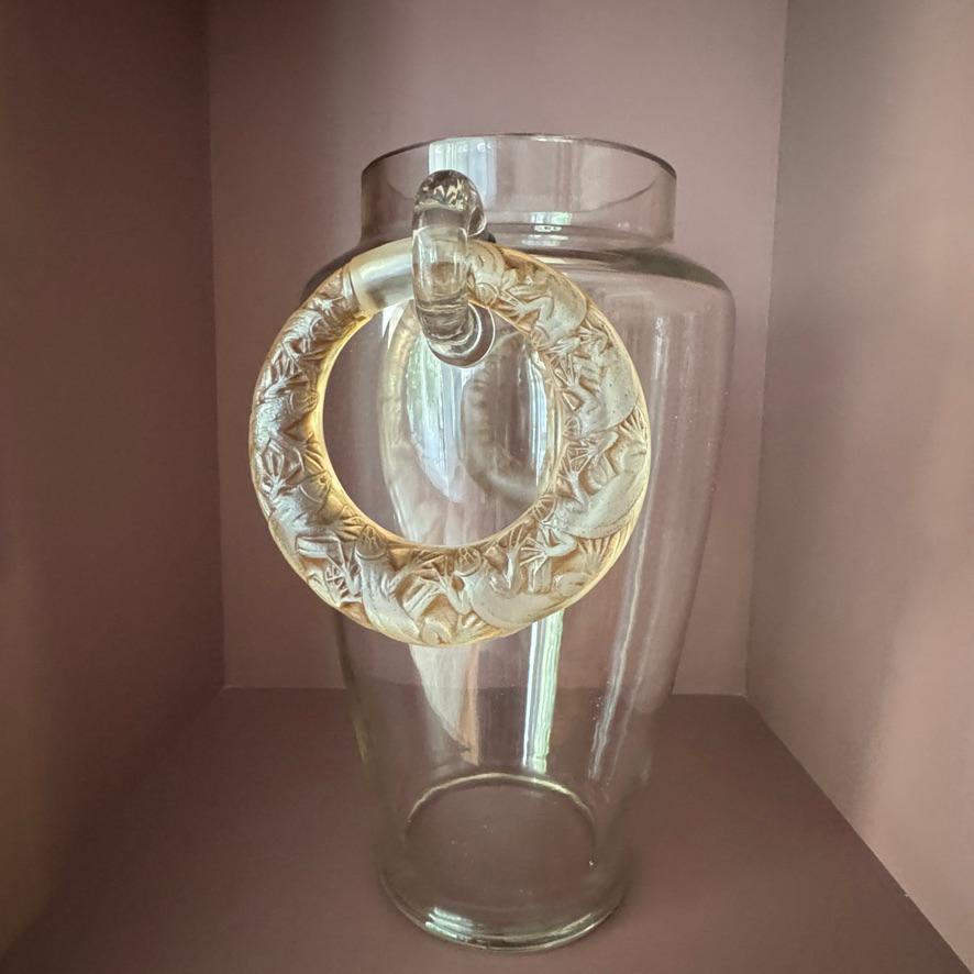 Questo vaso a 2 manici di Lézards è molto particolare nell'ampio inventario di vasi di R.Lalique.

Il corpo in vetro bianco è stato impreziosito da 2 applicazioni soffiate a mano in cui la decorazione  Le maniglie verranno posizionate.

Per tenerli