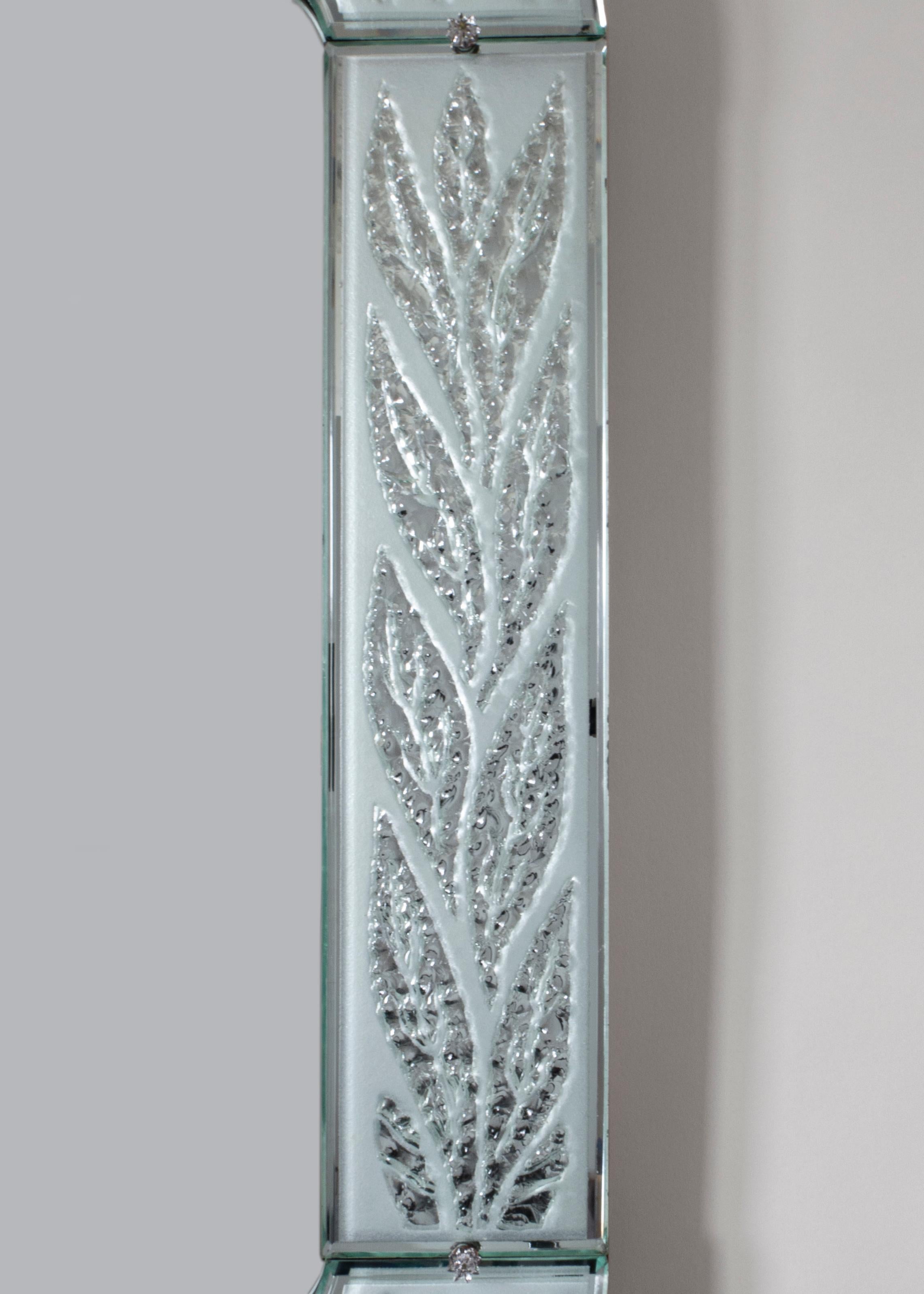 The rectangular mirror plate with rounded corners, within a conforming frame of chiseled and frosted glass panels depicting foliate, each panel with a soft blue-green tint, the corner panels subtlety projecting inwards, fastened by metal clips and