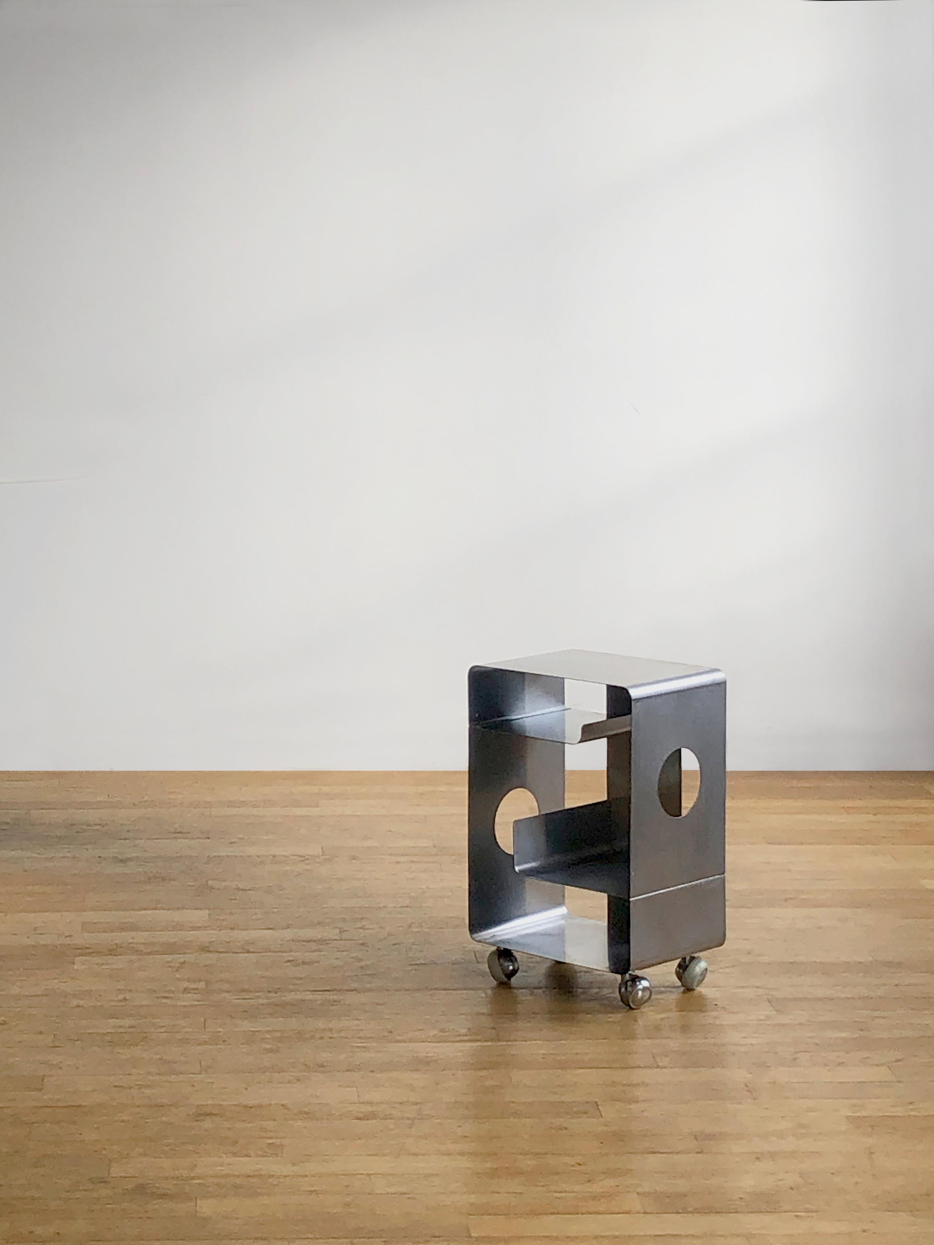 A rare and radical coffee table, side table, bedside table, or end table on wheels, Post-Modernist, Radical, Space Age, Seventies, featuring a geometric structure made of folded steel slats pierced by two circular openings on the sides, and two