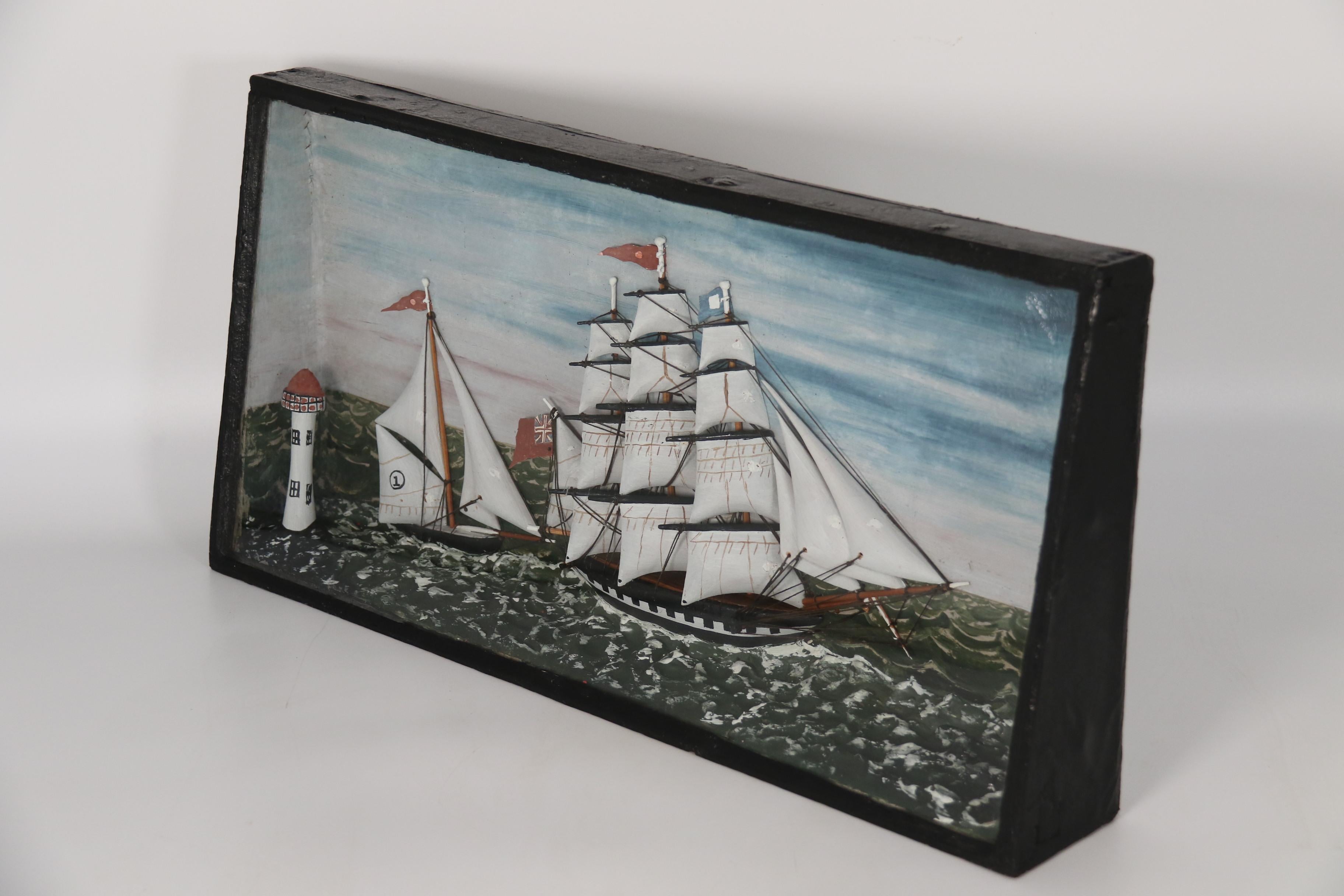 This most attractive mid 19th century folk art cased diorama shows a view at sea with a large three mast English ship being chased in a racing situation by a smaller and faster single mast yacht. Both are passing by a lighthouse which is in the