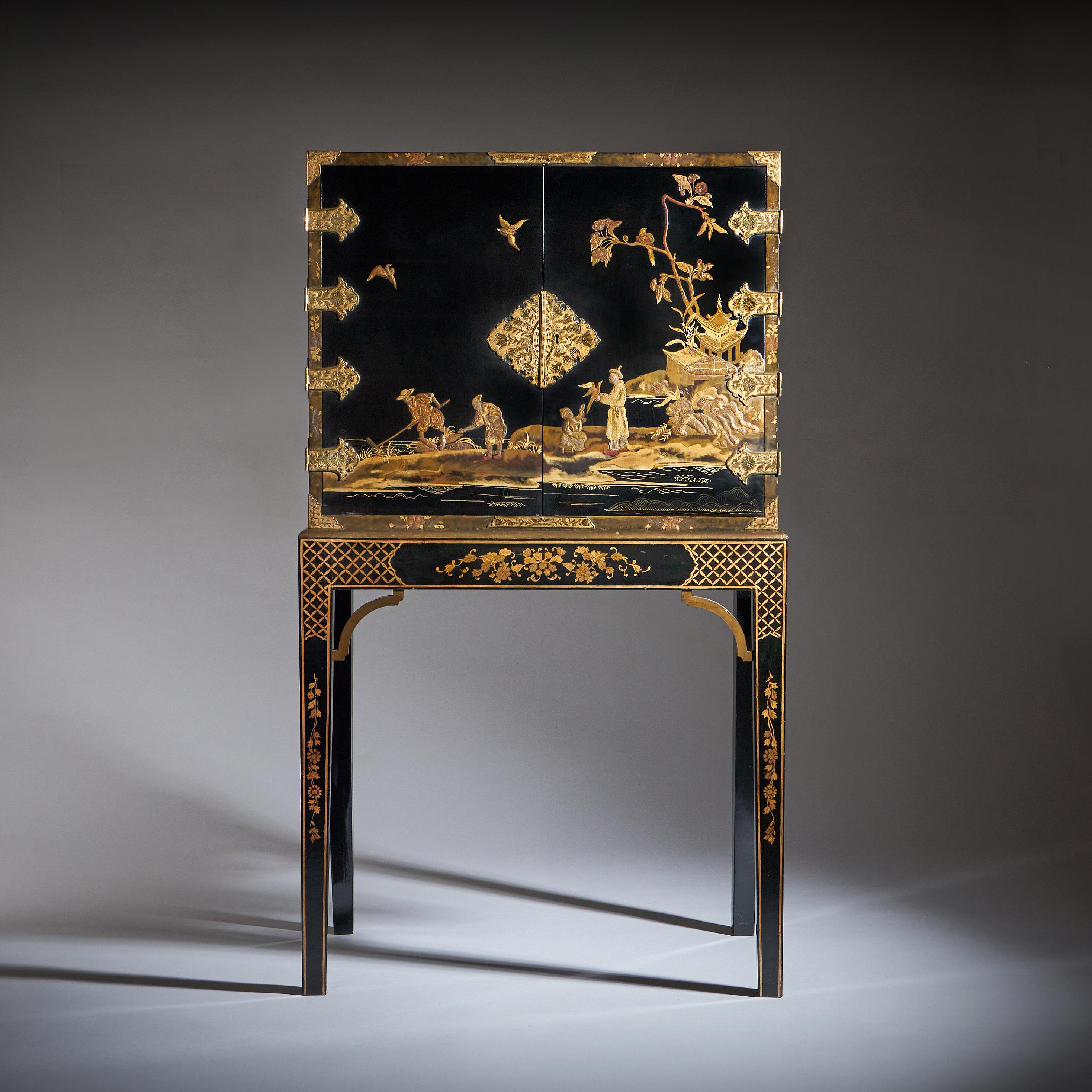 A beautifully ornate George III chinoiserie cabinet. The cabinet features a black lacquer finish with detailed artwork that contrasts beautifully against the dark background. This is a hallmark of the chinoiserie style, emphasizing opulence and