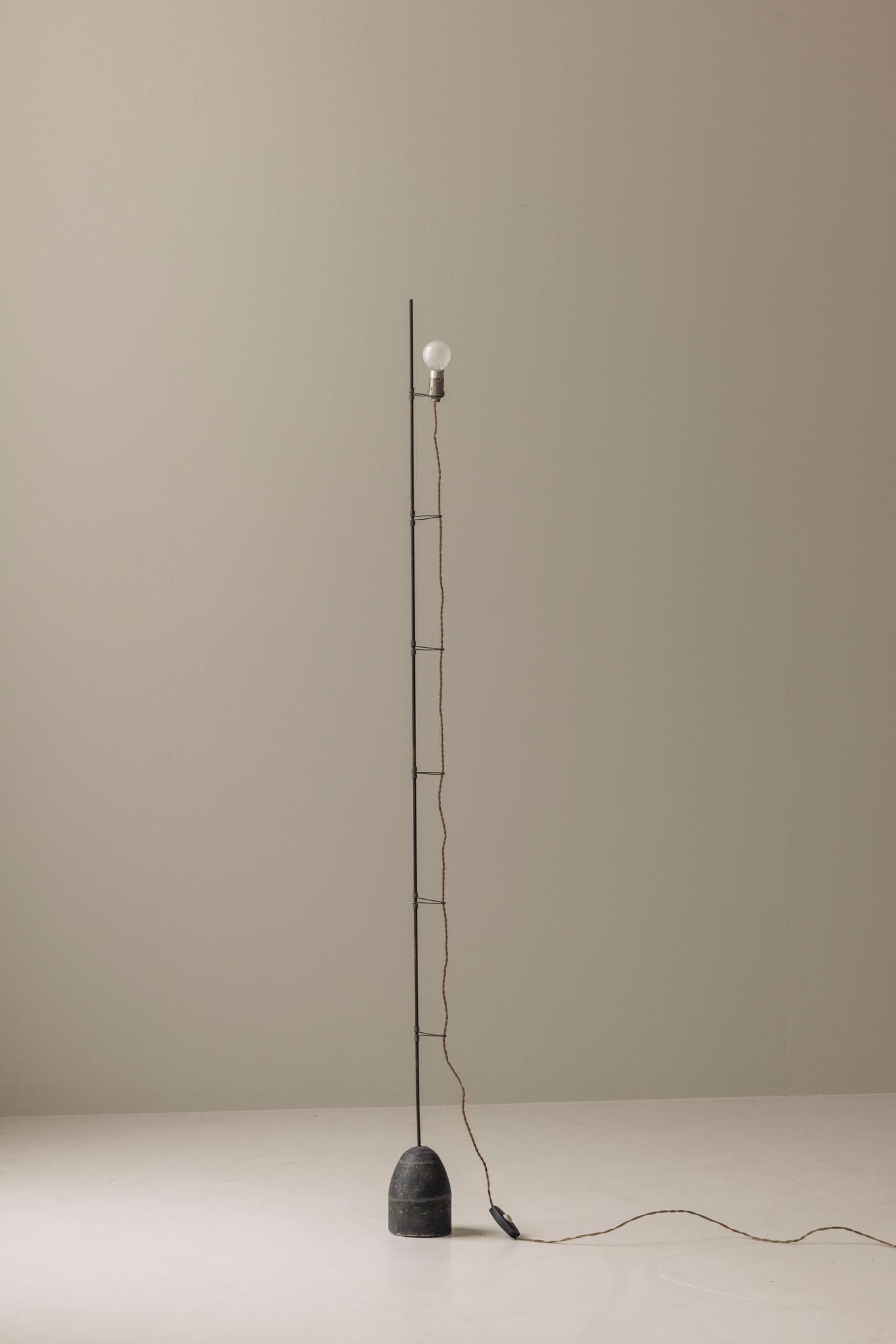 A rare and likely one-off floor lamp sourced in France, dating from the 1950s, combining brutalist charm with minimalist design. This sculptural piece features a solid concrete base, lending both visual weight and stability, paired with a slender
