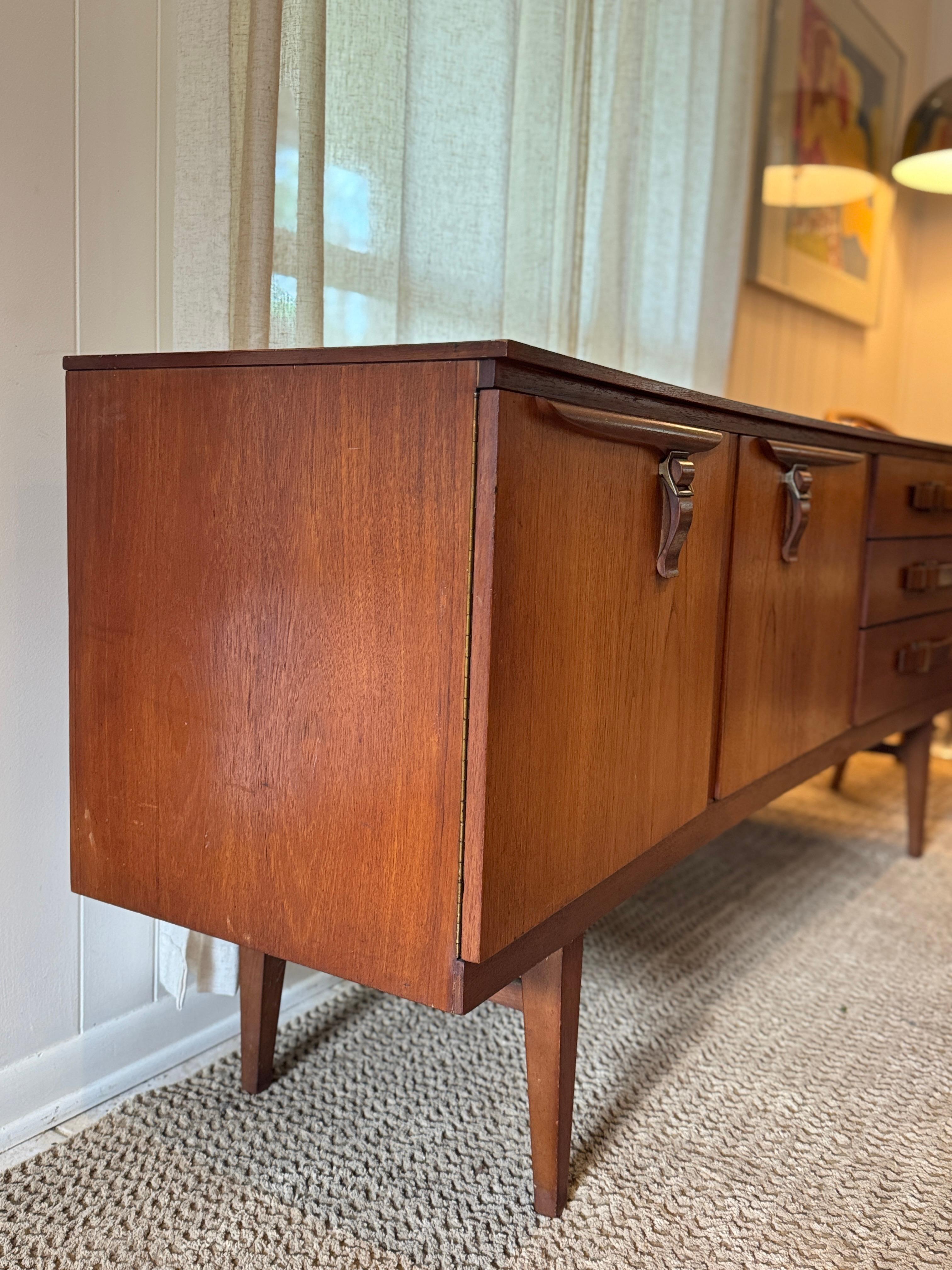 A rare and stunning mid century modern sideboard by Beautility, circa 1950s. This exceptional piece showcases the timeless elegance of the era with its sleek, streamlined silhouette and distinctive belt style handles, a hallmark of thoughtful
