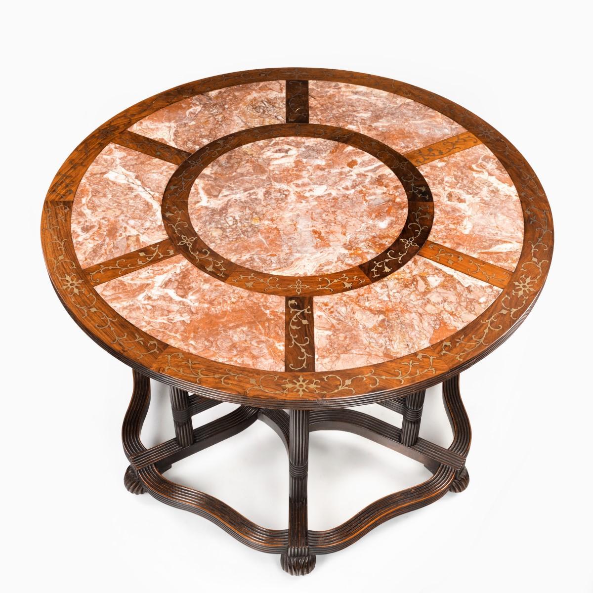 A rare Anglo-Chinese hardwood picnic table, in three sections, the circular top inlaid with six rouge marble segments centred on a roundel, the frame inlaid in brass with delicate leafy scrolls, the six reeded legs centred on a carved knot boss and