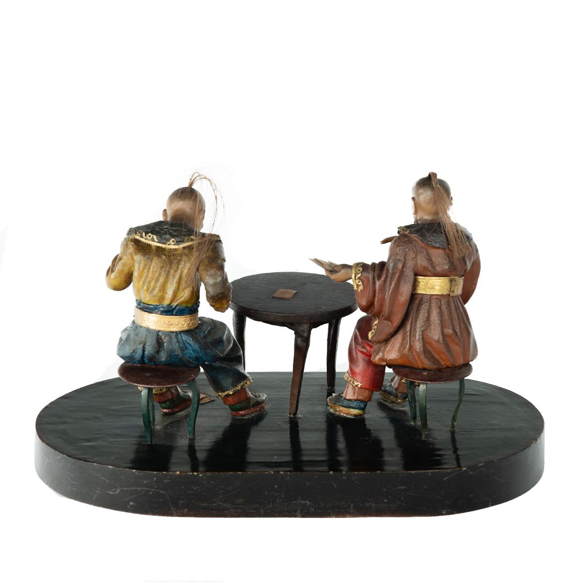 A rare Anglo-Chinese Regency polychrome painted wax and wood group of two Chinese card players, both with nodding heads with horsetail top-knots, wearing jackets with large collars, one with wide-sleeves,  gilt belts and voluminous trousers, seated