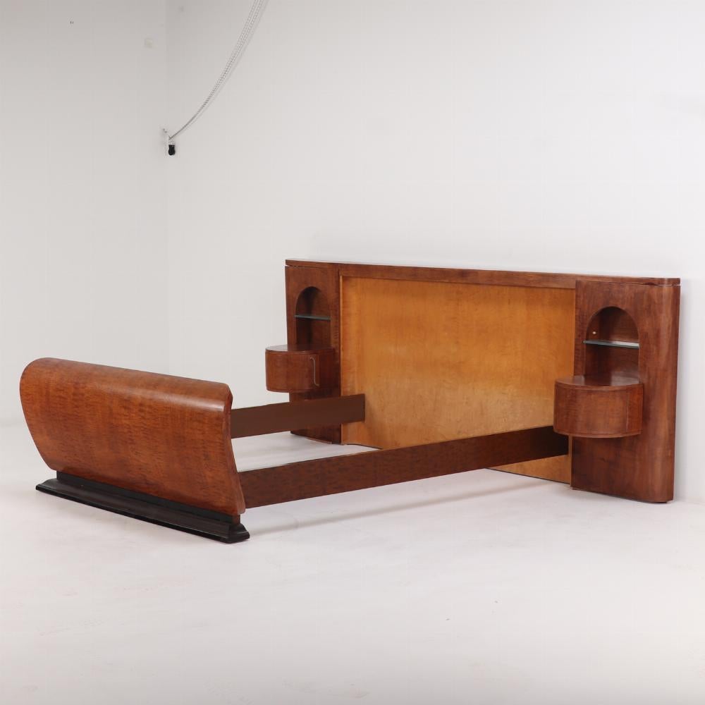 A rare find in the form of a queen size Art Deco satinwood bed with night stands, C 1930. The rectangular headboard done in satinwood flanked by two arched niches containing half-round drum cabinets with nickel-plated steel pulls and glass shelves