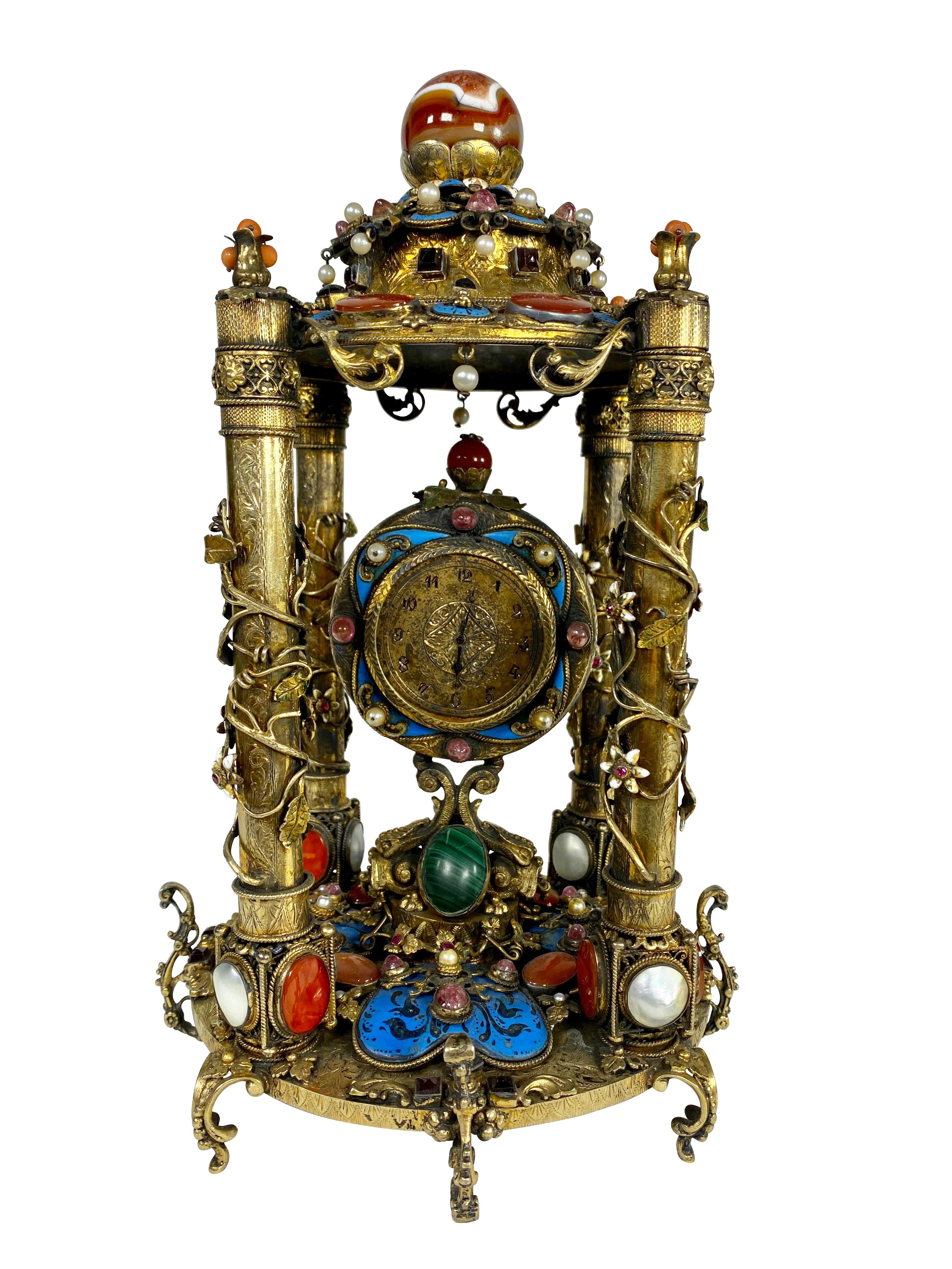 A Rare Austro Hungarian Gilt Silver & Jeweled Table Clock, Circa 1900, having semi precious stones throughout including agate, malachite, amethyst, pearl, coral and enamel DIMENSIONS: HEIGHT: 11 DIAMETER 7