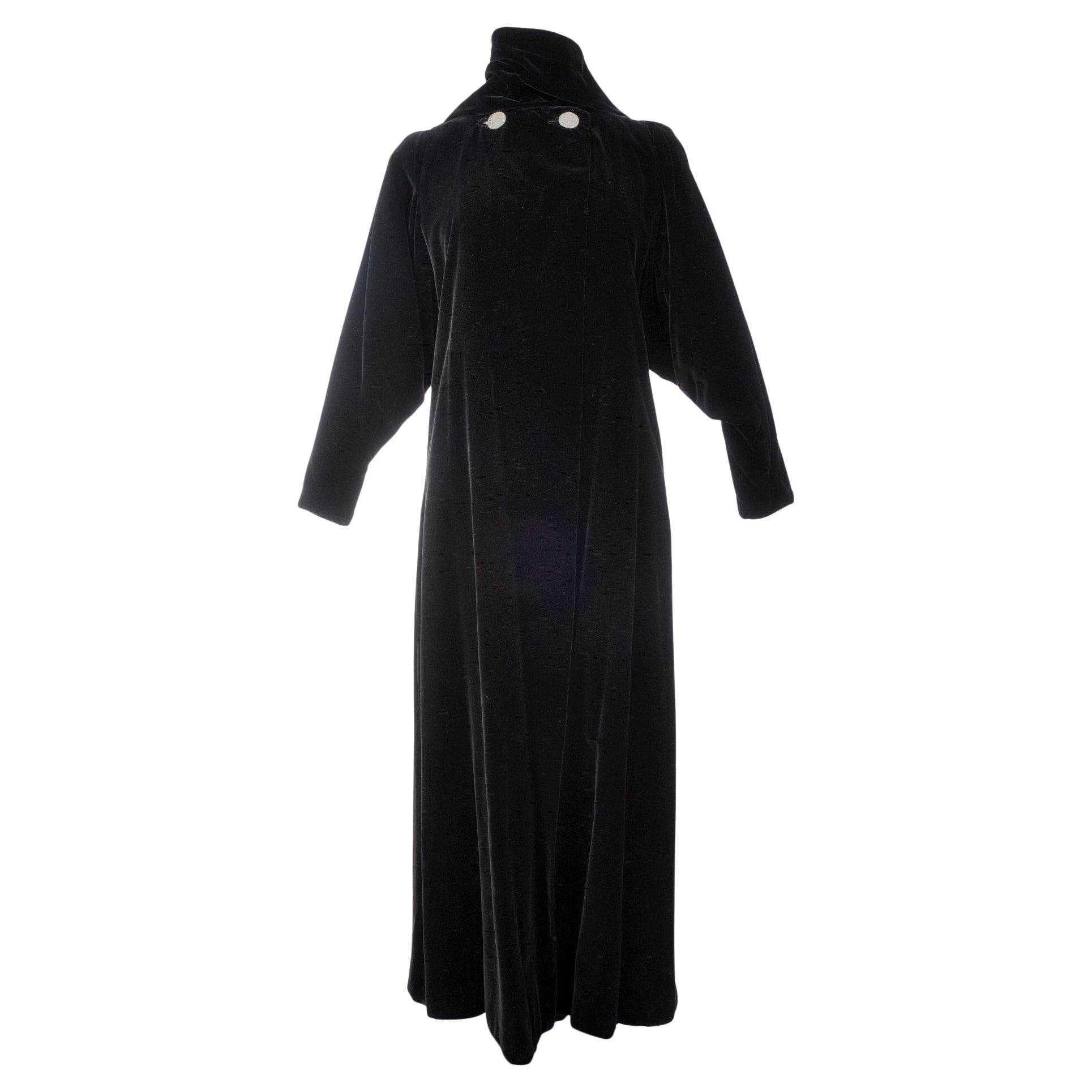 Vers 1937
France pour l'exportation États-Unis ou Angleterre

Long manteau du soir en velours de soie noir, foulard à nouer sur le col fermé par deux gros boutons en strass, doublure en satin duchesse, Label Reproduction Lucien Lelong, Paris. Il