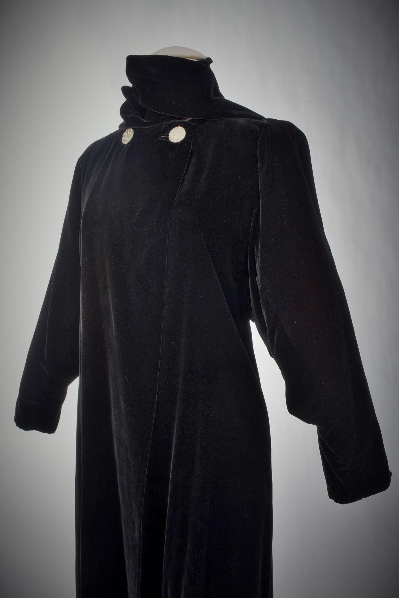 Circa 1937

France for Export United States or England

Long evening coat in black silk velvet, scarf to tie on the collar closed by two large rhinestone buttons, duchesse satin lining, Labelled Reproduction Lucien Lelong, Paris. This is a license