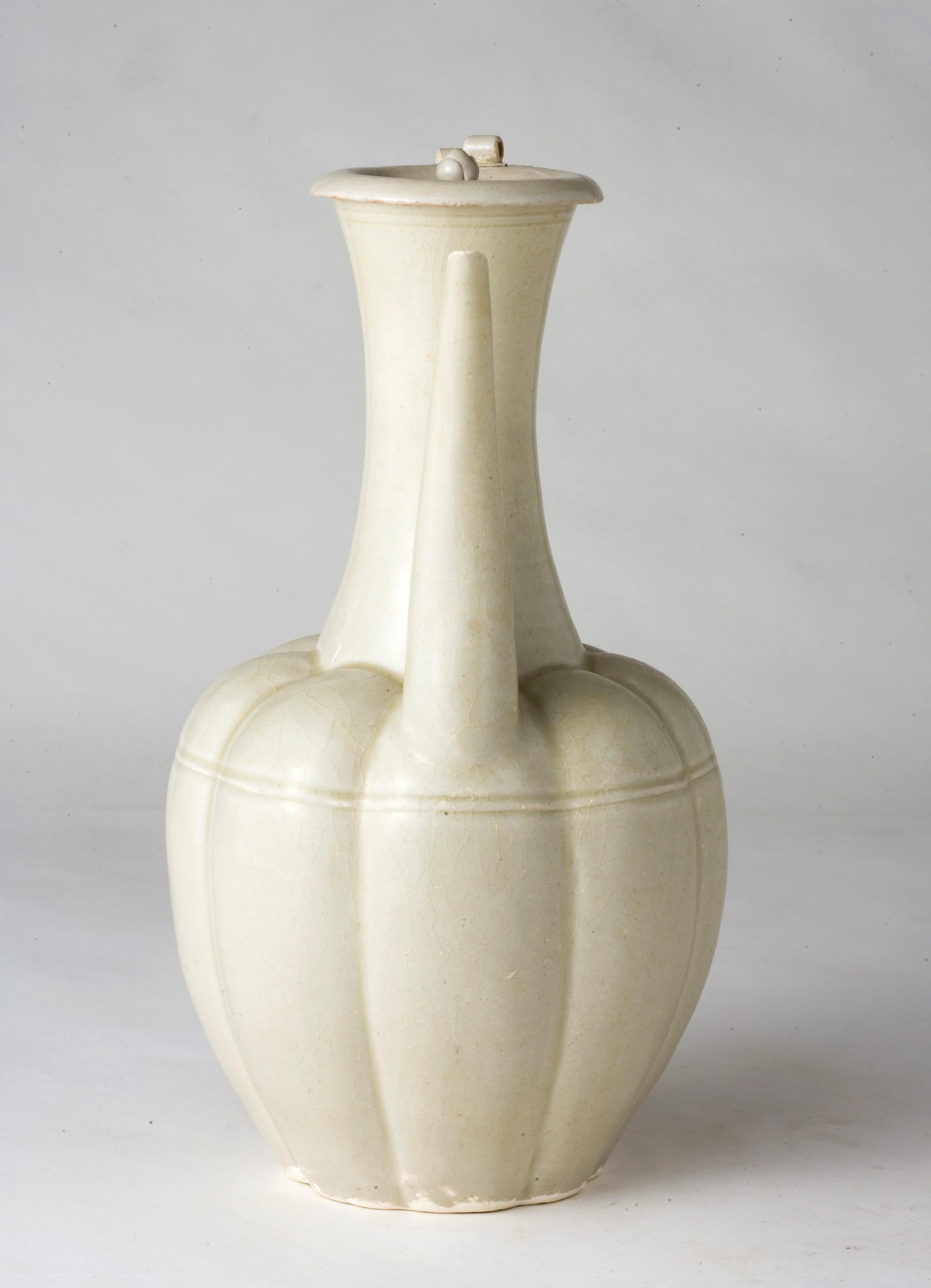 The octagonal lobed ovoid body rising from a short spreading foot to a tall trumpet neck, set at the shoulder with a tall curved spout and to the other side with a tall strap handle, the dished cover surmounted with a ruyi-shaped finial, covered