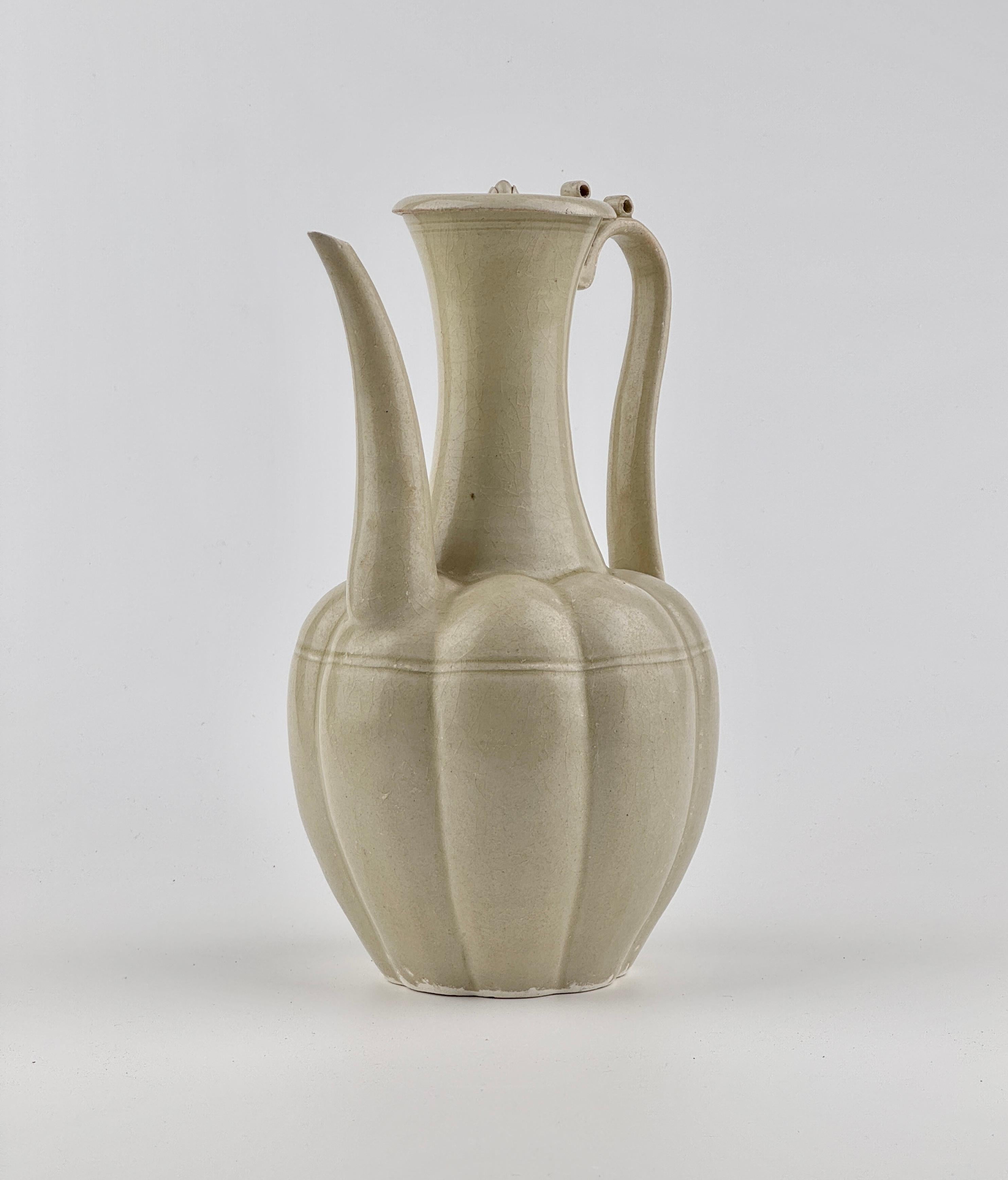 The octagonal lobed ovoid body rising from a short spreading foot to a tall trumpet neck, set at the shoulder with a tall curved spout and to the other side with a tall strap handle, the dished cover surmounted with a ruyi-shaped finial, covered