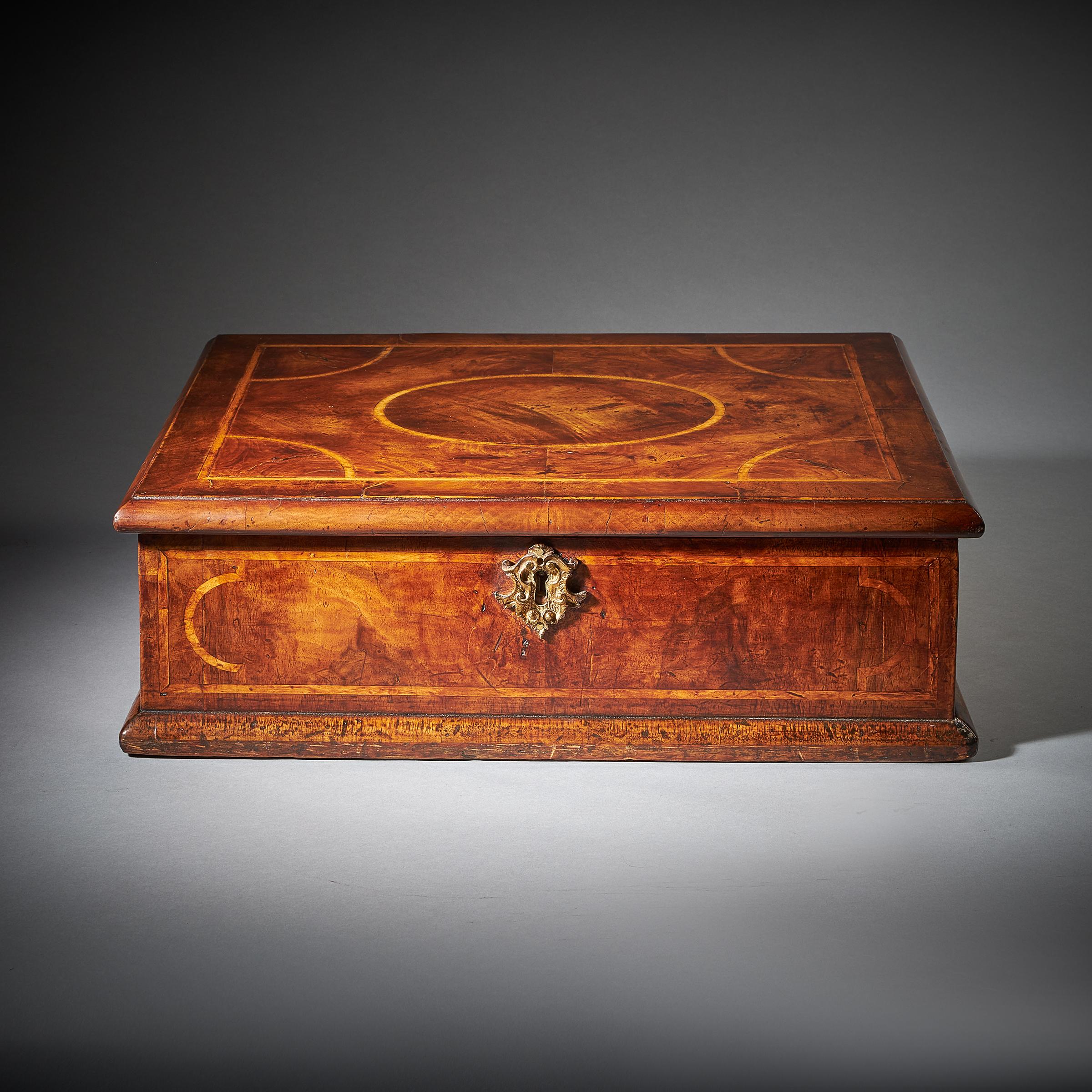 A rare figured walnut Queen Anne - George I period lace box, circa 1700-1720. 

The cross-grain banded ovolo moulded top is veneered in figured walnut consisting of an oval to the centre and a quadrant to each corner inlaid in holly. 

The