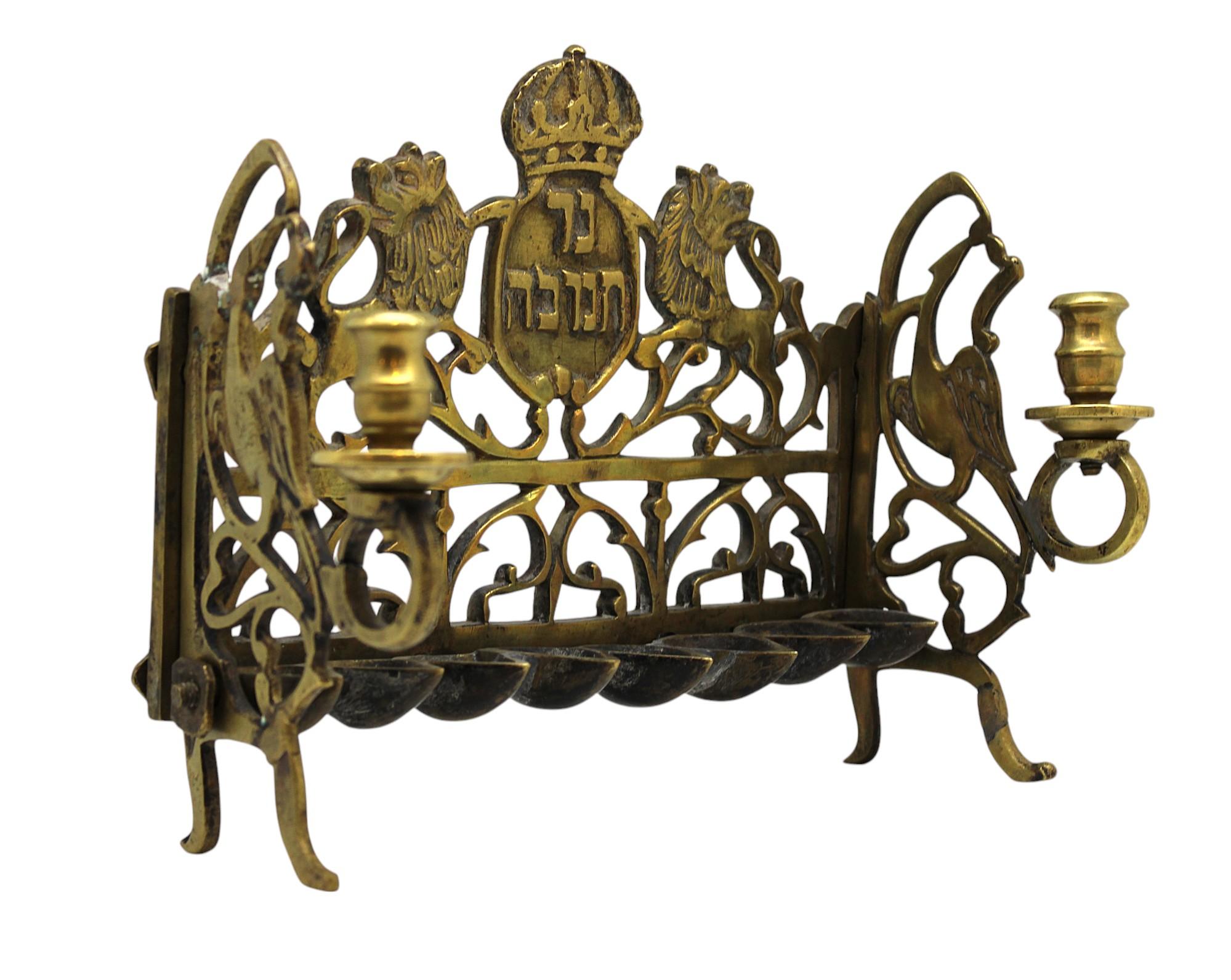 Questa rara lampada di Hanukkah in ottone della Galizia, realizzata in Polonia intorno al 1800, è uno squisito esempio di arte cerimoniale ebraica. La lampada presenta un design simmetrico e traforato con dettagli intricati caratteristici