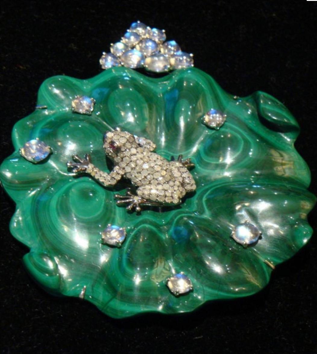The Following Items we are offering is An Outstanding 18 Karat White Gold, Malachite, Diamond, Moonstone and Ruby Water Lily Pendant/Objet, consisting of a carved fluted malachite plaque in a lily pad motif surmounted with a central black rhodium