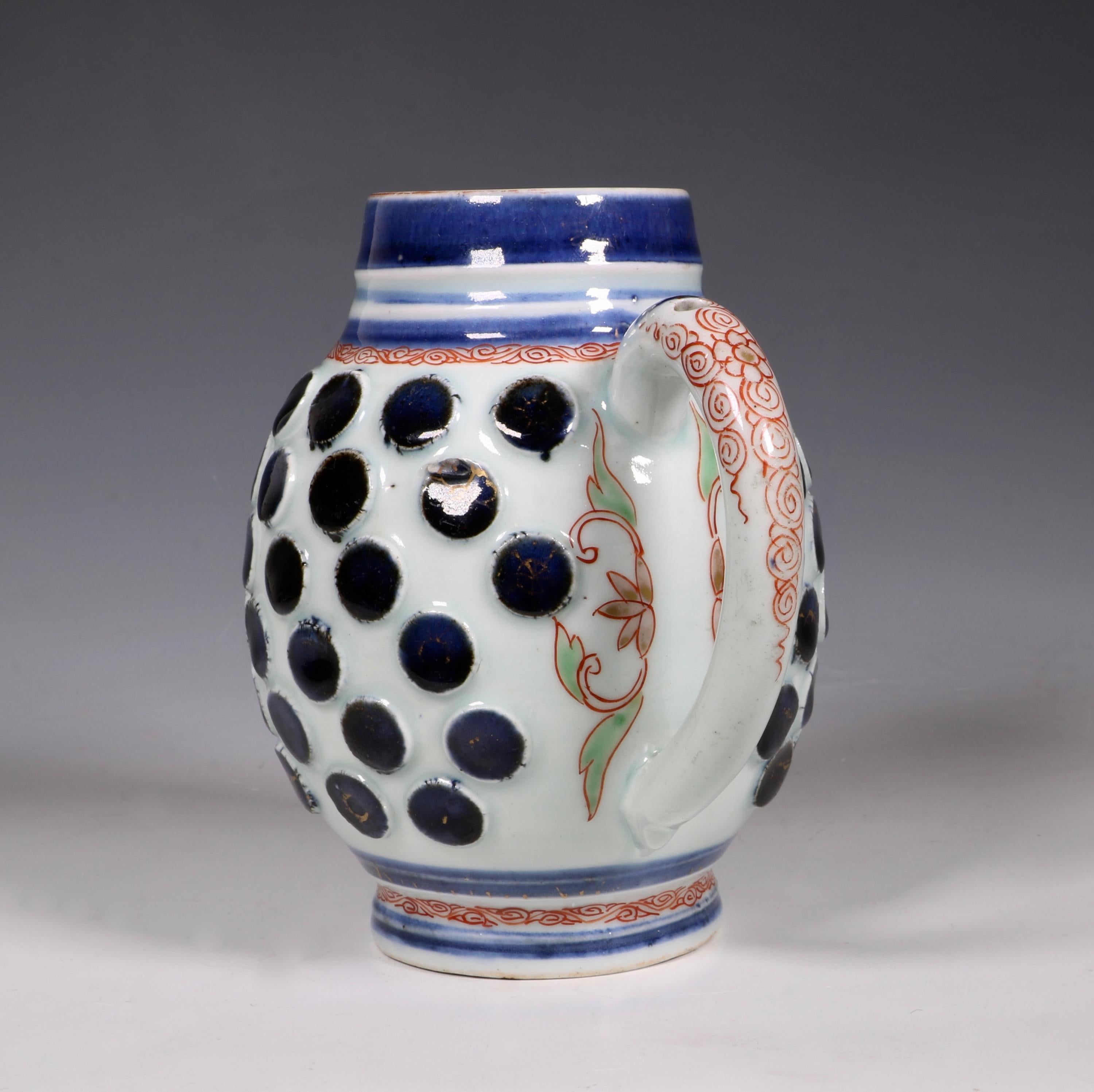 A rare Japanese Arita Tankard. After a German stoneware, probably Westerwald late 17th century original. The rounded body applied with round bosses painted blue.

The ribbed neck with blue bands. Traces of gilt. Japanese Arita, circa