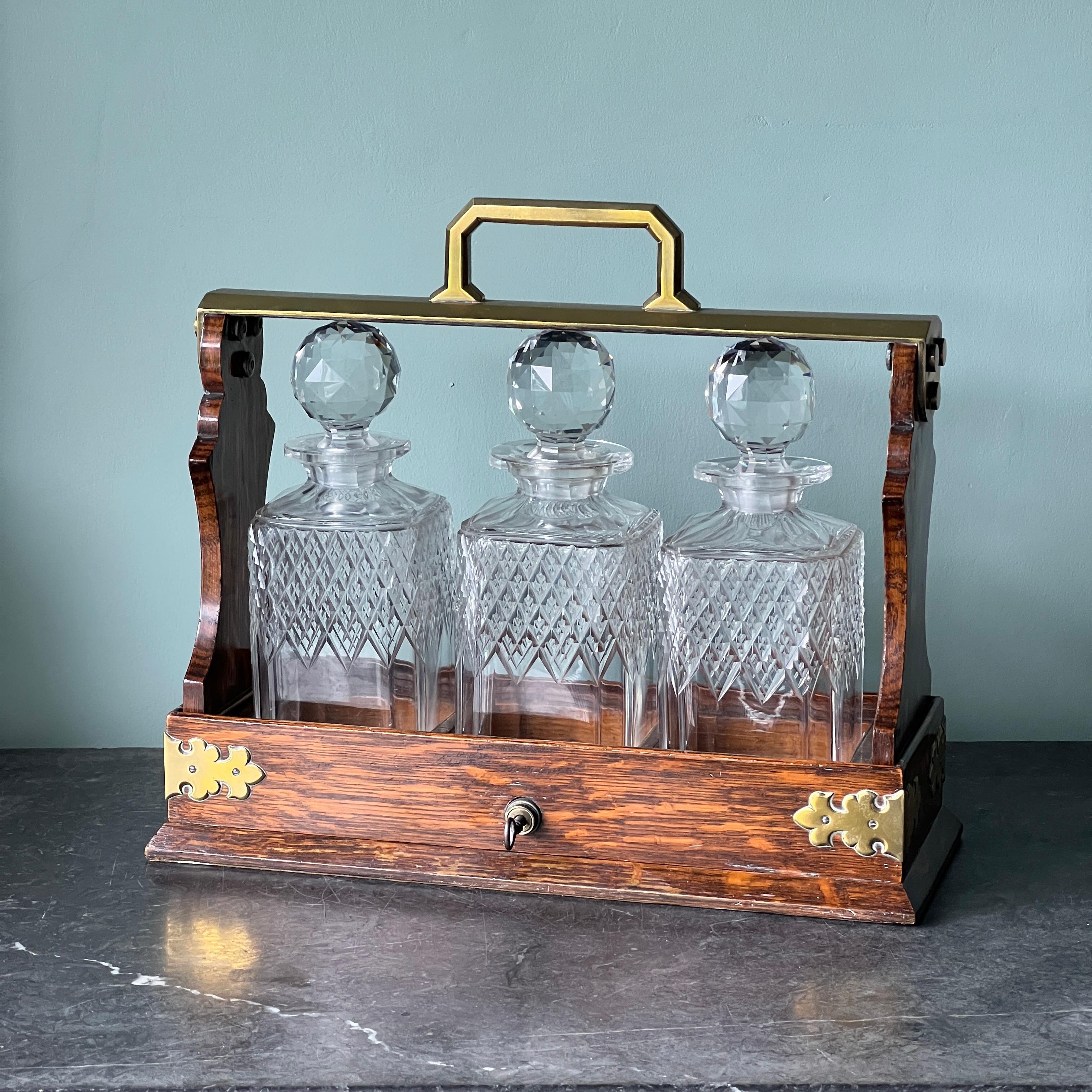 A Lovely Mappin and Webb Victorian Oak and Brass Tantalus from around 1880. Crafted with precision and care, this piece boasts a sturdy brass handle attached to elegant oak columns adorned with charming brass accents. The base features intricately