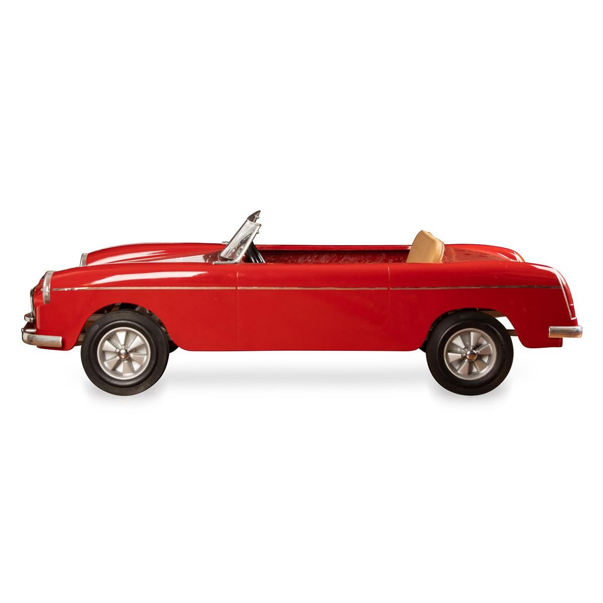 A late-20th Century English made “MG“ model pedal car, red fiberglass molded body with tan vinyl upholstery, mounted on square section steel chassis, treadle pedals to cranked rear axle, plastic windscreen and with solid rubber tyres. In excellent,