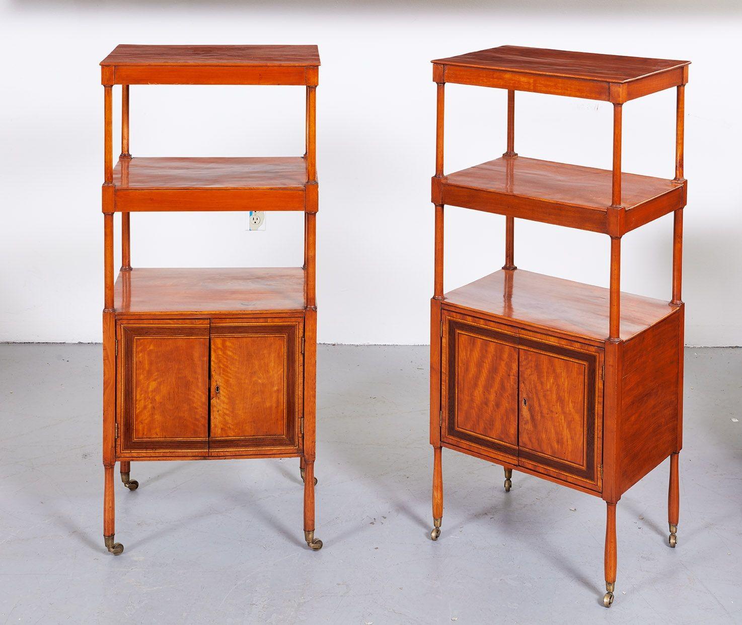 A rare pair of etageres in wonderfully grained satinwood having classically shaped columns supporting top and middle shelves with aprons over a base shelf cupboard with double doors with fine string border inlay, all on shaped legs ending in brass