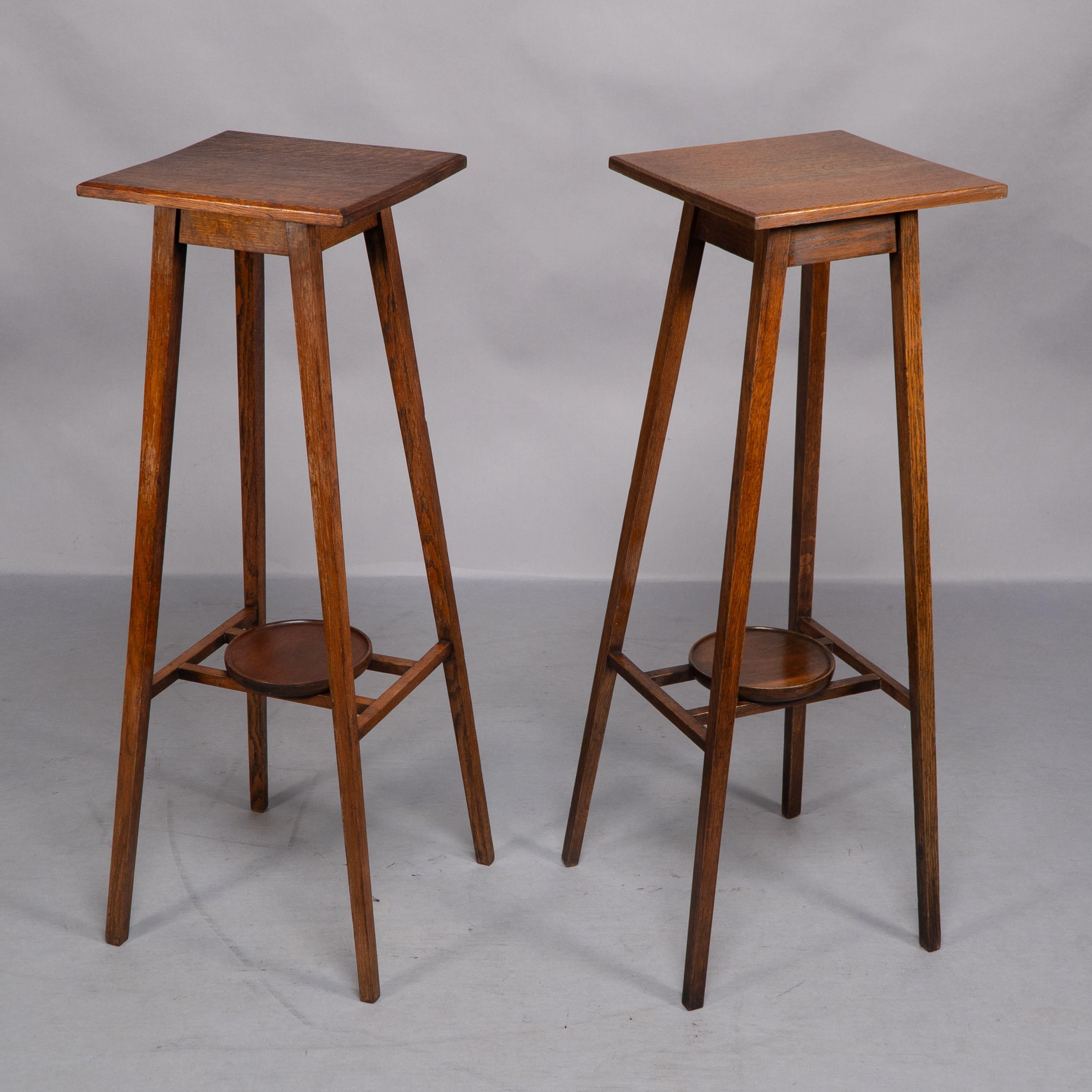 Una rara coppia di semplici piantane in legno di quercia Arts and Crafts con piani quadrati e gambe affusolate unite in basso da due barelle gemelle con un portapiante circolare sopra (i portapiante sono in noce). See: Mobili per buoni cittadini di
