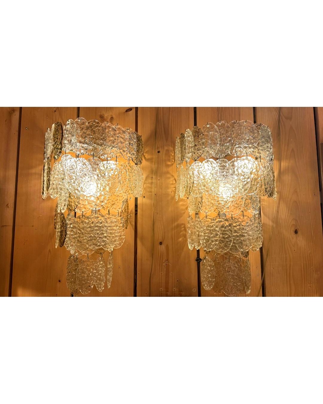 Raro par de apliques de pared en cascada, atribuidos a Gino Vistosi (1925-1980), fabricados en Murano, Venecia.
Cada aplique está compuesto por colgantes ovalados de cristal de efecto martillado en tonos claros y ahumados, que crean un refinado