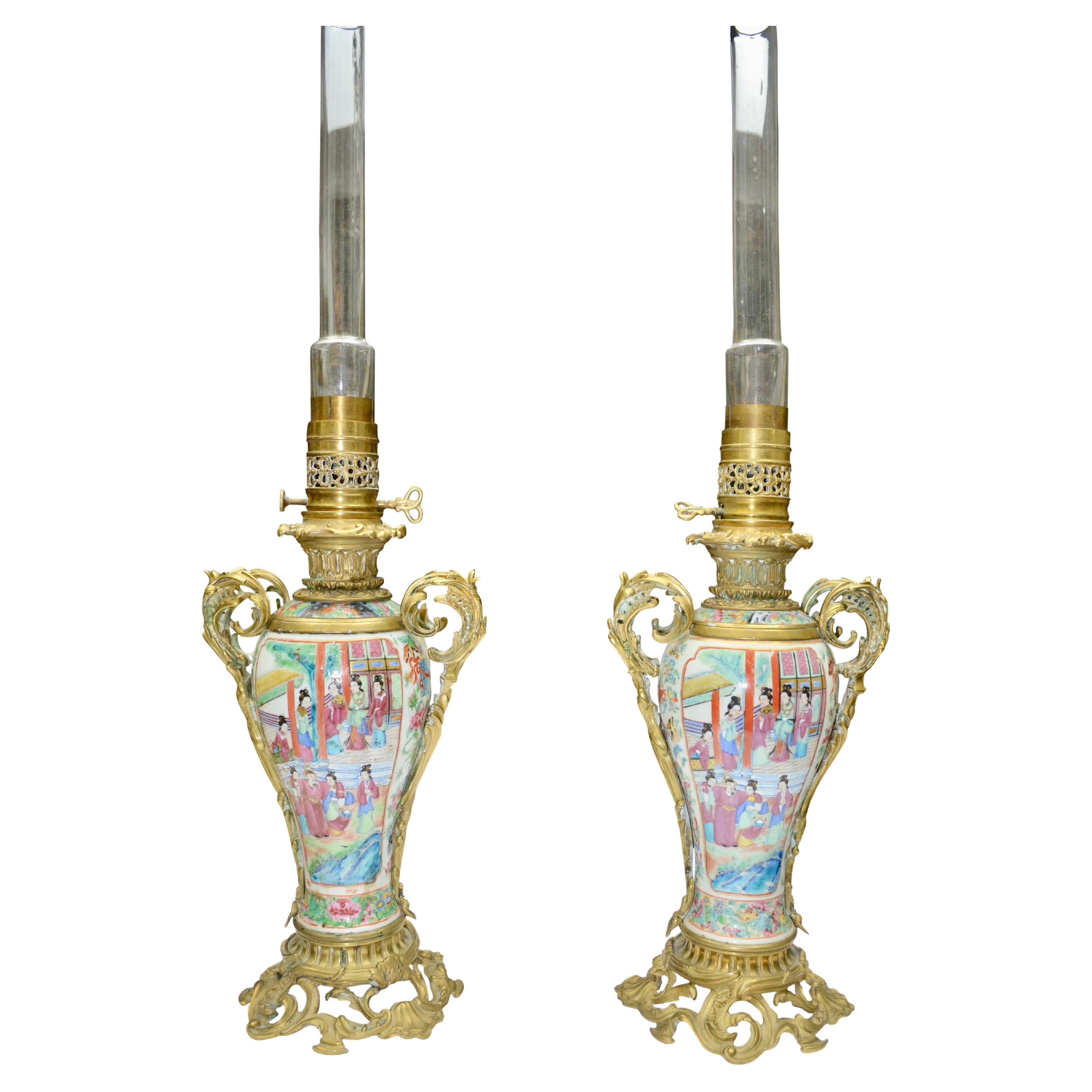 A beautiful French and Asian collaboration of a 19th century pair of Napoleon III Famille Rose porcelain gilt bronze and brass oil lamps that miraculously include the original glass tube shades. . The lamps are raised on an elegant round rococo