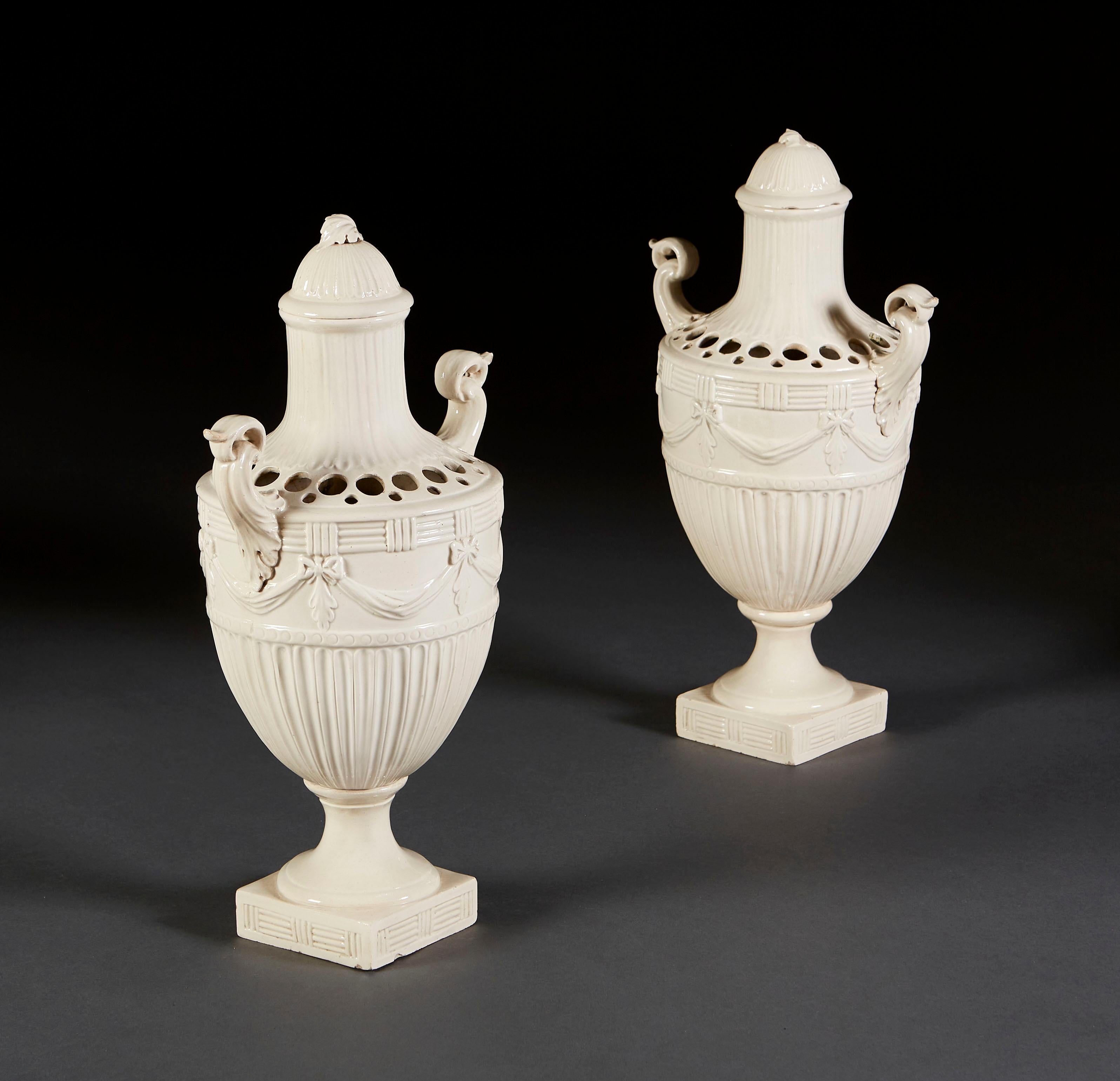 A fine pair of large creamware vases or tuliperies, of fluted urn form with scroll handles and swag decoration below pierced trumpet tops, the domed covers with twisted leaf decoration, all standing on waisted socles with square bases.