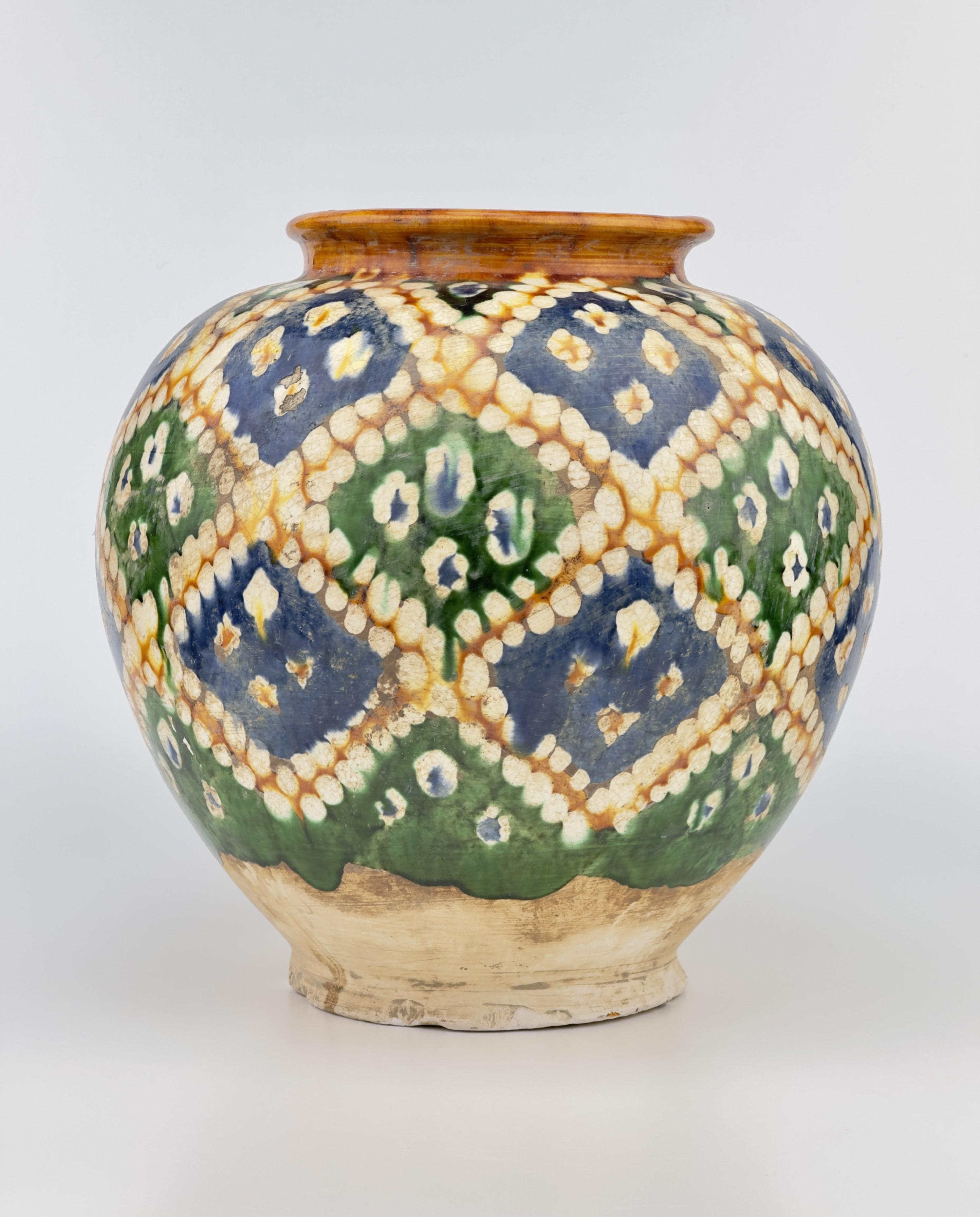 The jar is of globular shape and is decorated to the body with a geometric design band of lozenge-shaped motifs in blue, green, ochre and cream below a plain ochre everted mouth rim, all above an unglazed base.

The rainbow-like colors on this