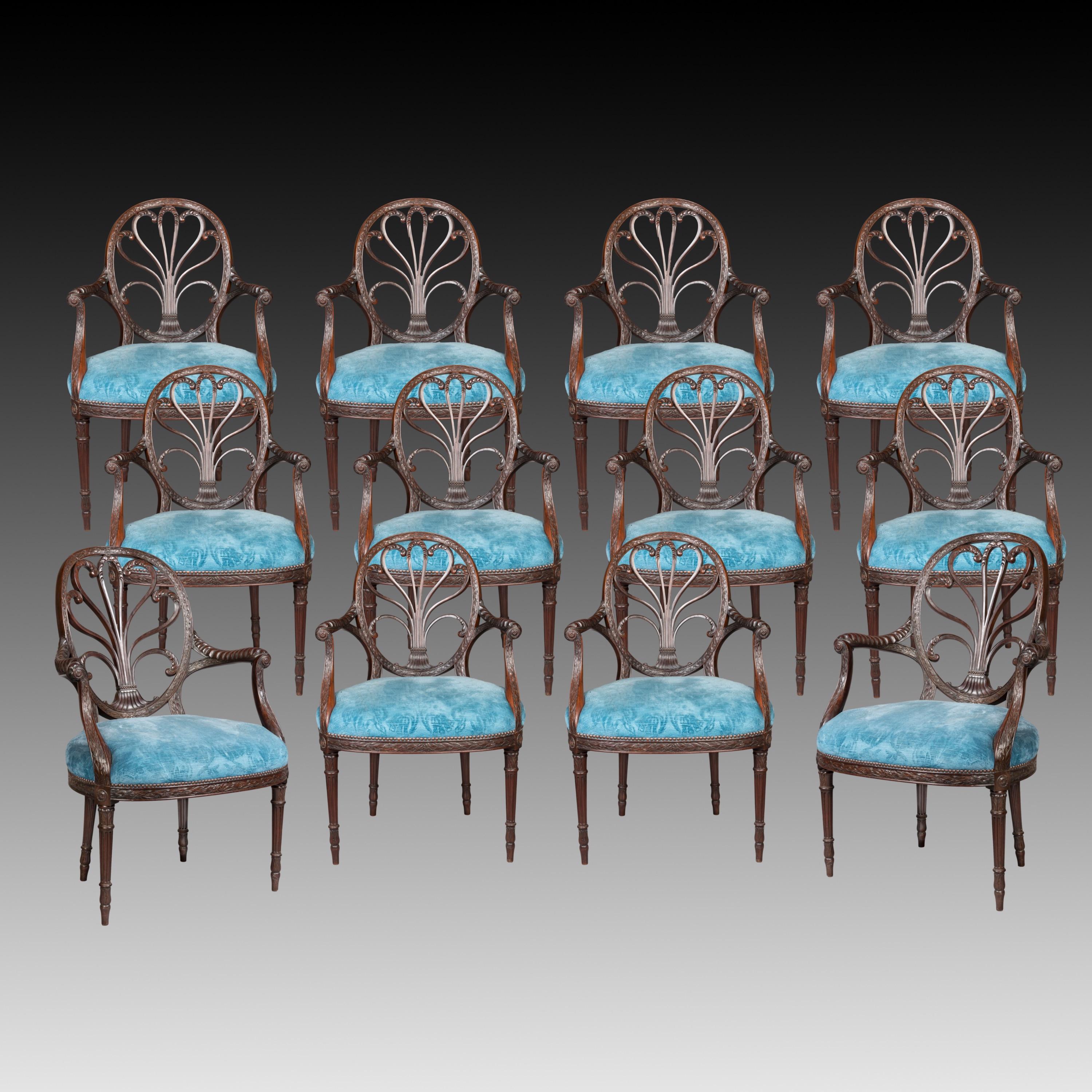 A rare set of beautifully drawn proportions with two larger armchairs and ten of smaller scale, all carved from mahogany, rising from tapering and fluted ring turned front legs, with bands of palm fronds atop, and canted rear legs; the bowed front