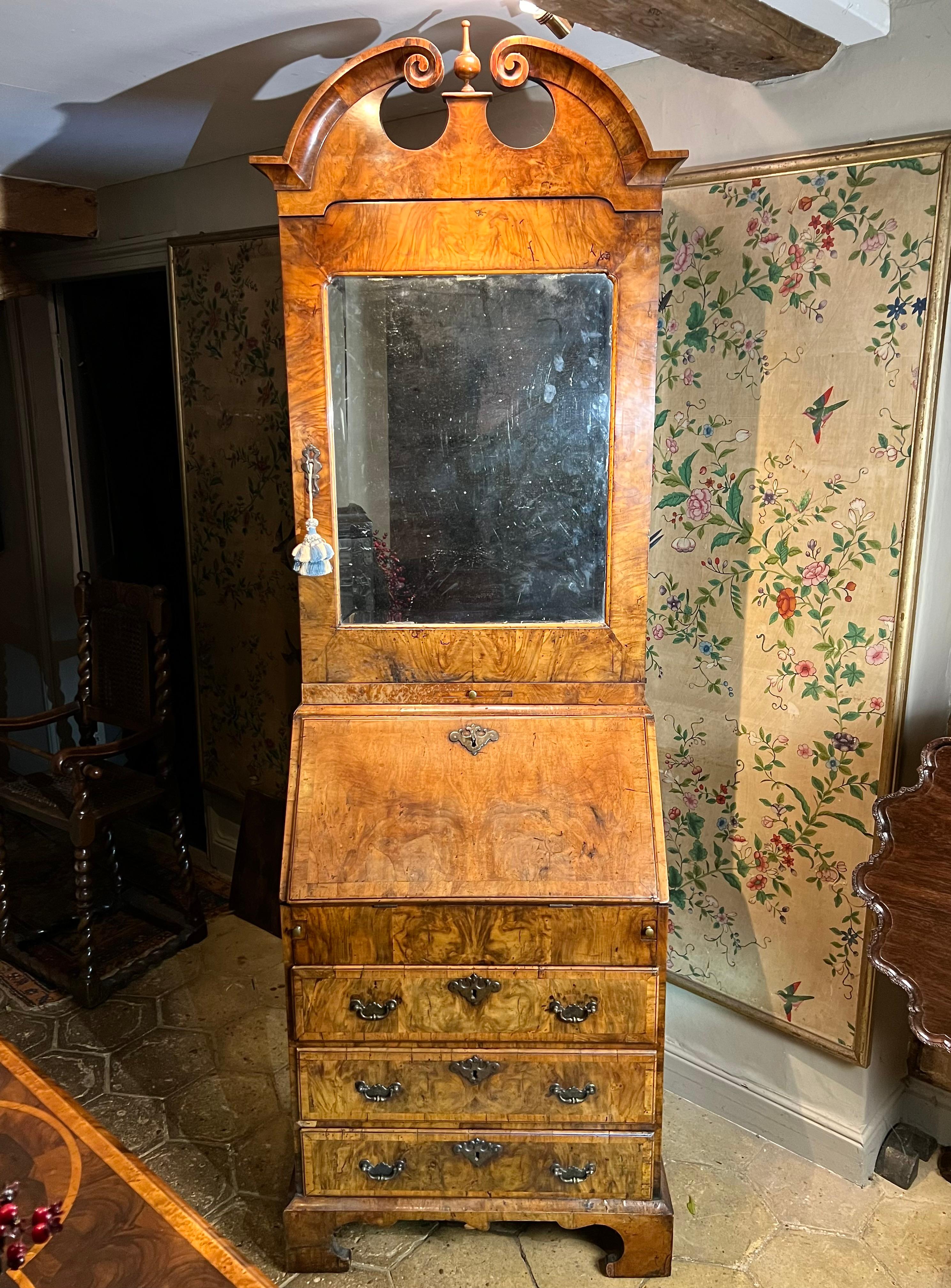 Rare petite armoire-bureau en noyer d'époque George I / II, avec un fronton mouluré en col de cygne. Vers 1727-1730.

La plaque de miroir biseautée est munie d'une glissière pour bougie.
La partie inférieure de l'écritoire, derrière la chute, révèle