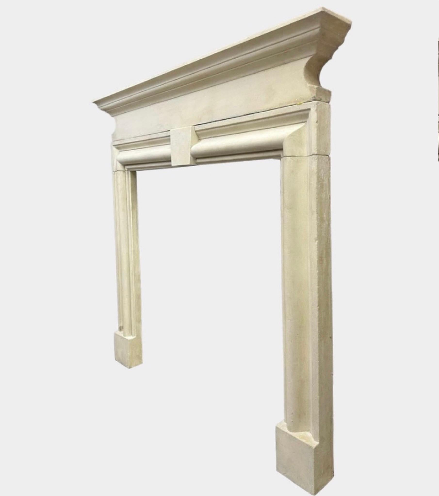 An English reclaimed stone fireplace in the 18th century manner. The bolection moulded jambs and frieze with plain incised keystone to centre. The C scrolled cushion moulding supporting a wide stepped shelf. Stood on square foot blocks. Dated from