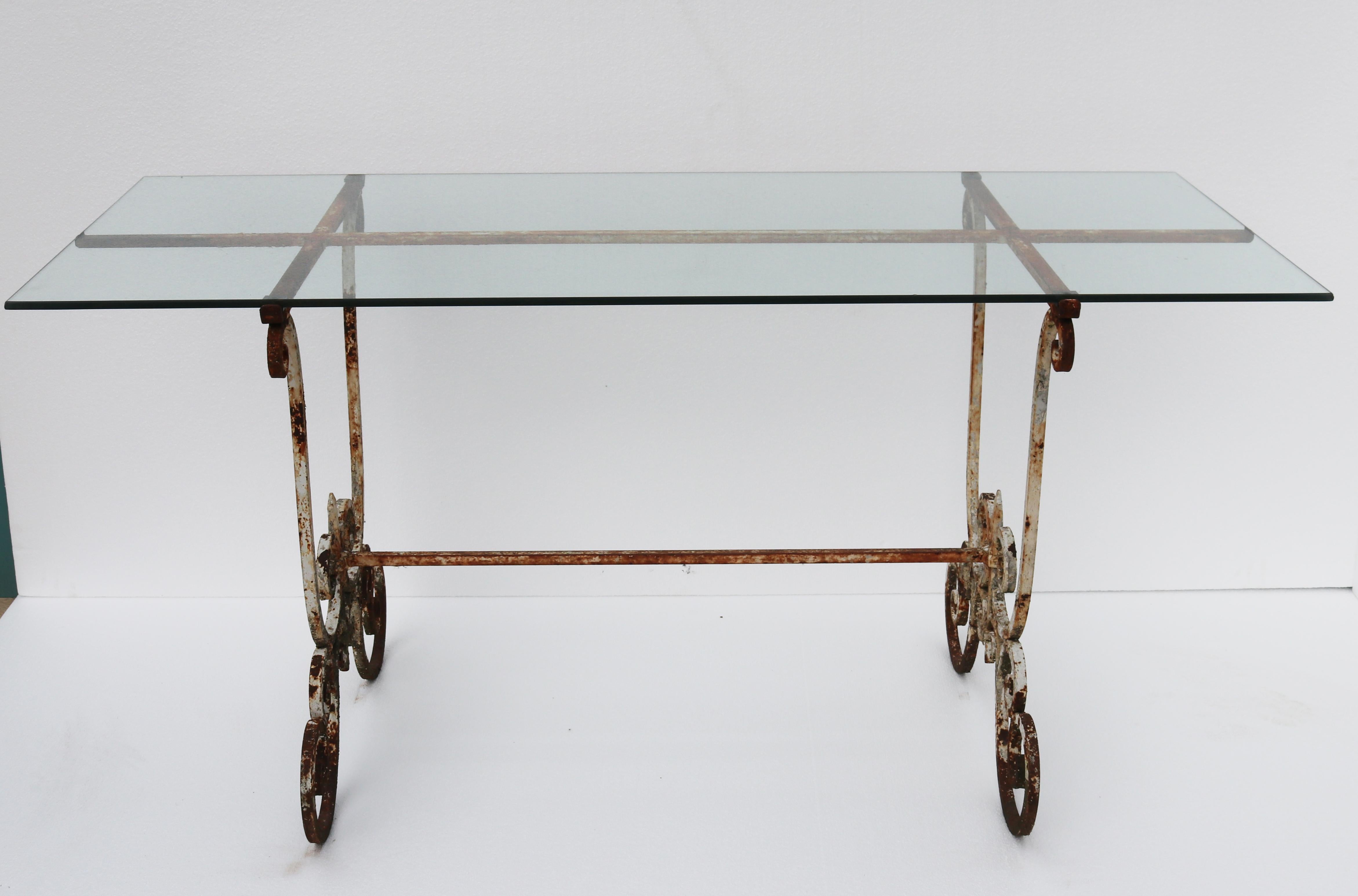 Eine Tischplatte aus Glas, die auf einem Eisengestell mit geschwungenem Muster ruht.