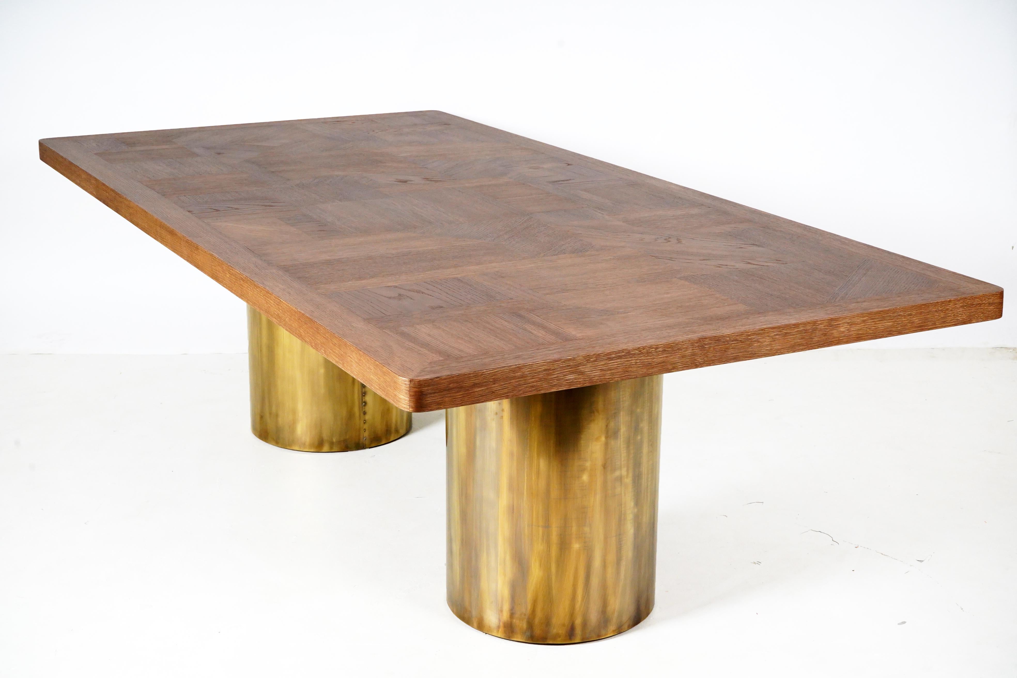 This large and sturdy oak parquet table top rests on large brass-wrapped cylinder-shaped legs. The thick oak tiles are held within a thick, solid oak frame. The top is lightly-textured with the grain left unfilled.  The unfilled grain is slightly