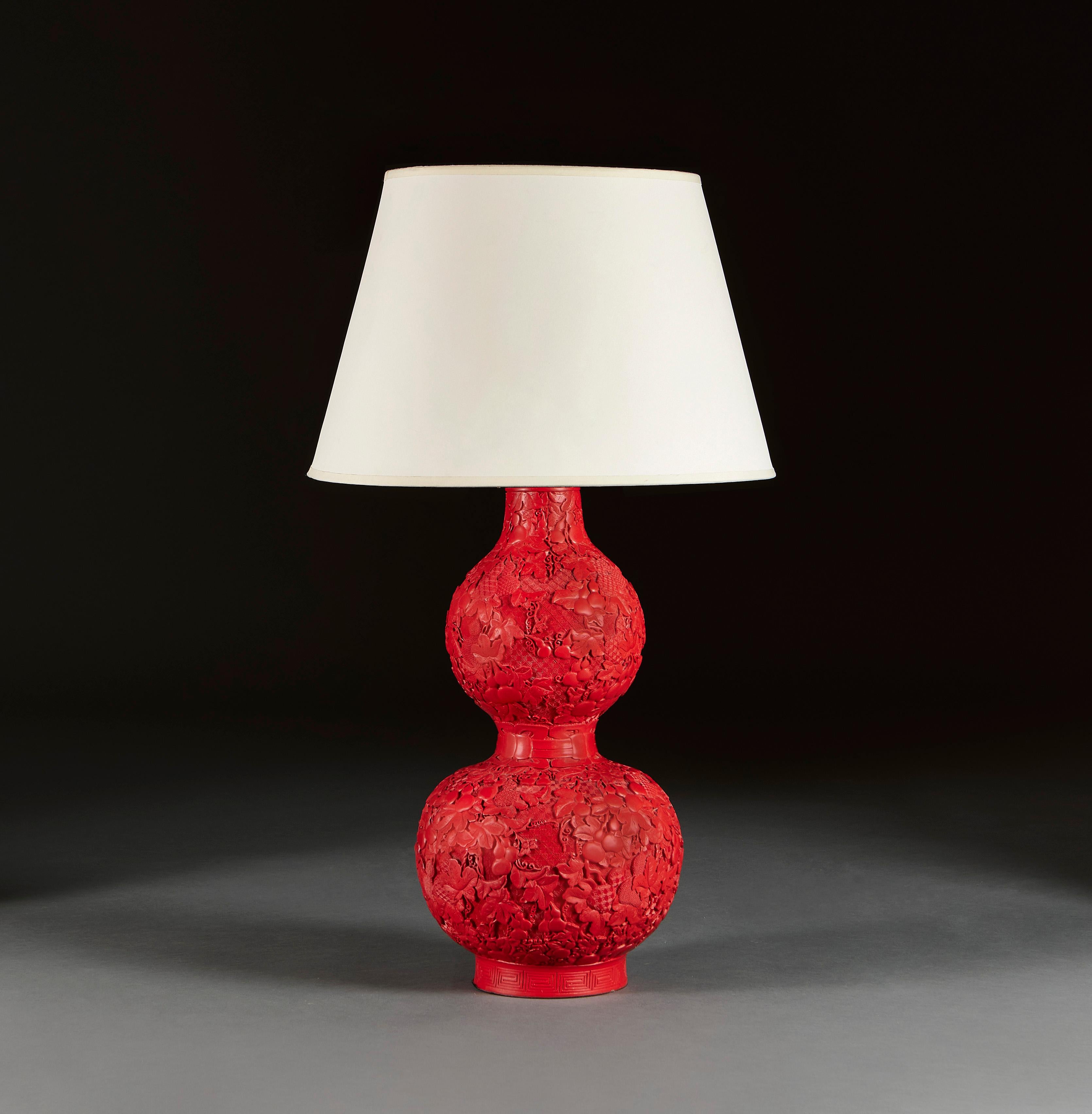 China, circa 1900

A large cinnabar lacquer vase in crimson red of double gourd form, with carvings of gourds and vine leaves, overlaid on a geometric cross hatched ground, now converted as a lamp.

Height of vase 50cm
Height with shade 79cm