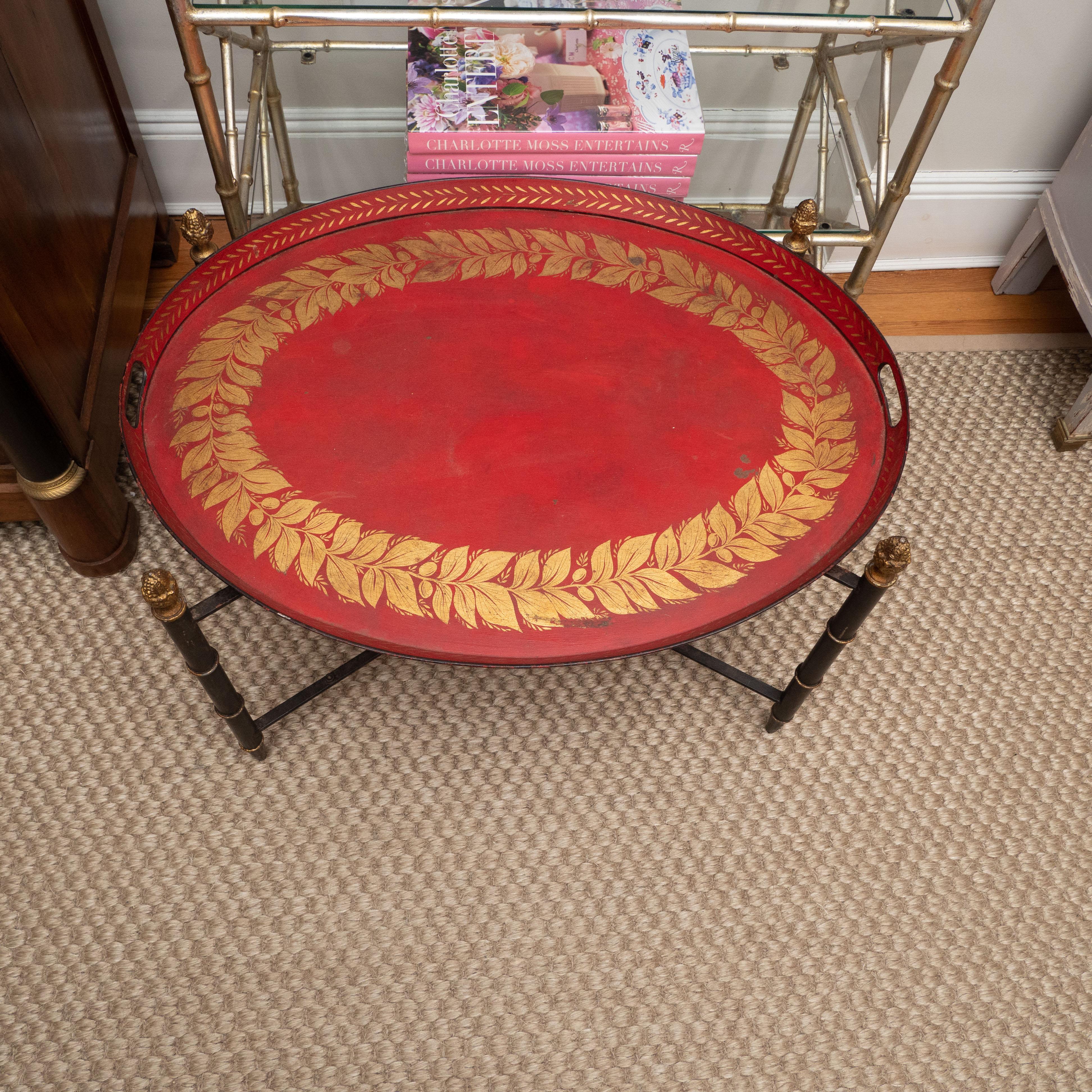 A lovely tole tray with a gallery in a custom stand. The tray, painted in a rich red, features a design painted in gold on top and sides. The X-frame stand has turned legs and acorn finials in gold. Perfect as a side table anywhere!