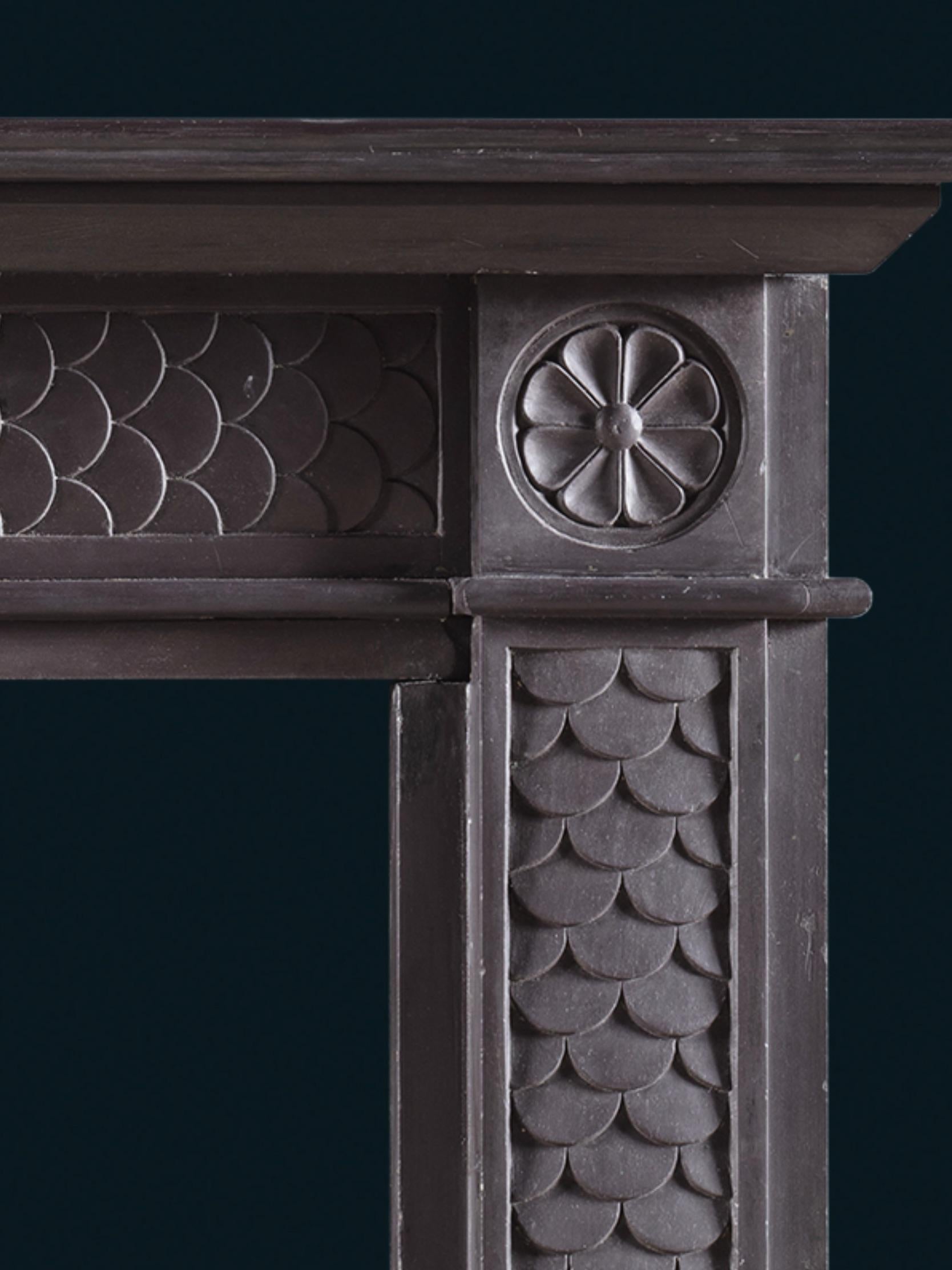 A fish-scale detail runs through the surround, and a patera motif is shown in the corner blocks and at centre of the header. The thin shelf together with the proportions of this design are typical of early 19th century chimneypieces, while the