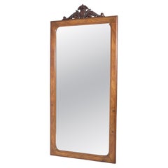 A refined wall mirror featuring a warm wooden frame with elegantly carved crest