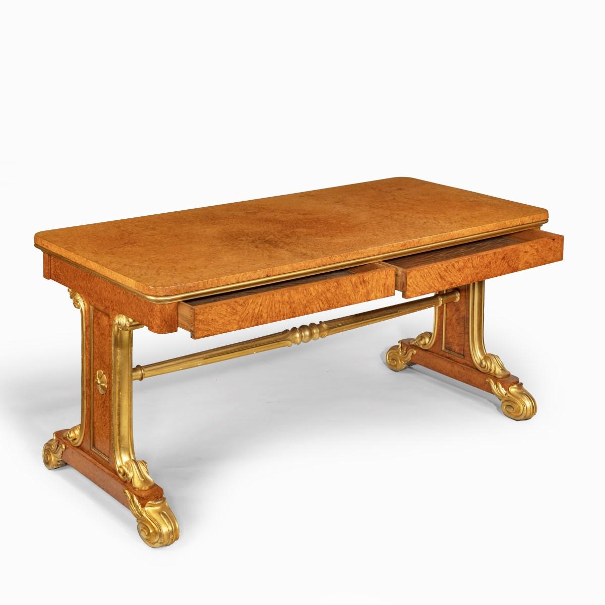 A Regency amboyna and gilt library table attributed to Seddon and Morel, with a rectangular top set upon solid end supports with a turned, reeded and gilded stretcher and gilded foliate scroll feet. It is decorated throughout with rich amboyna