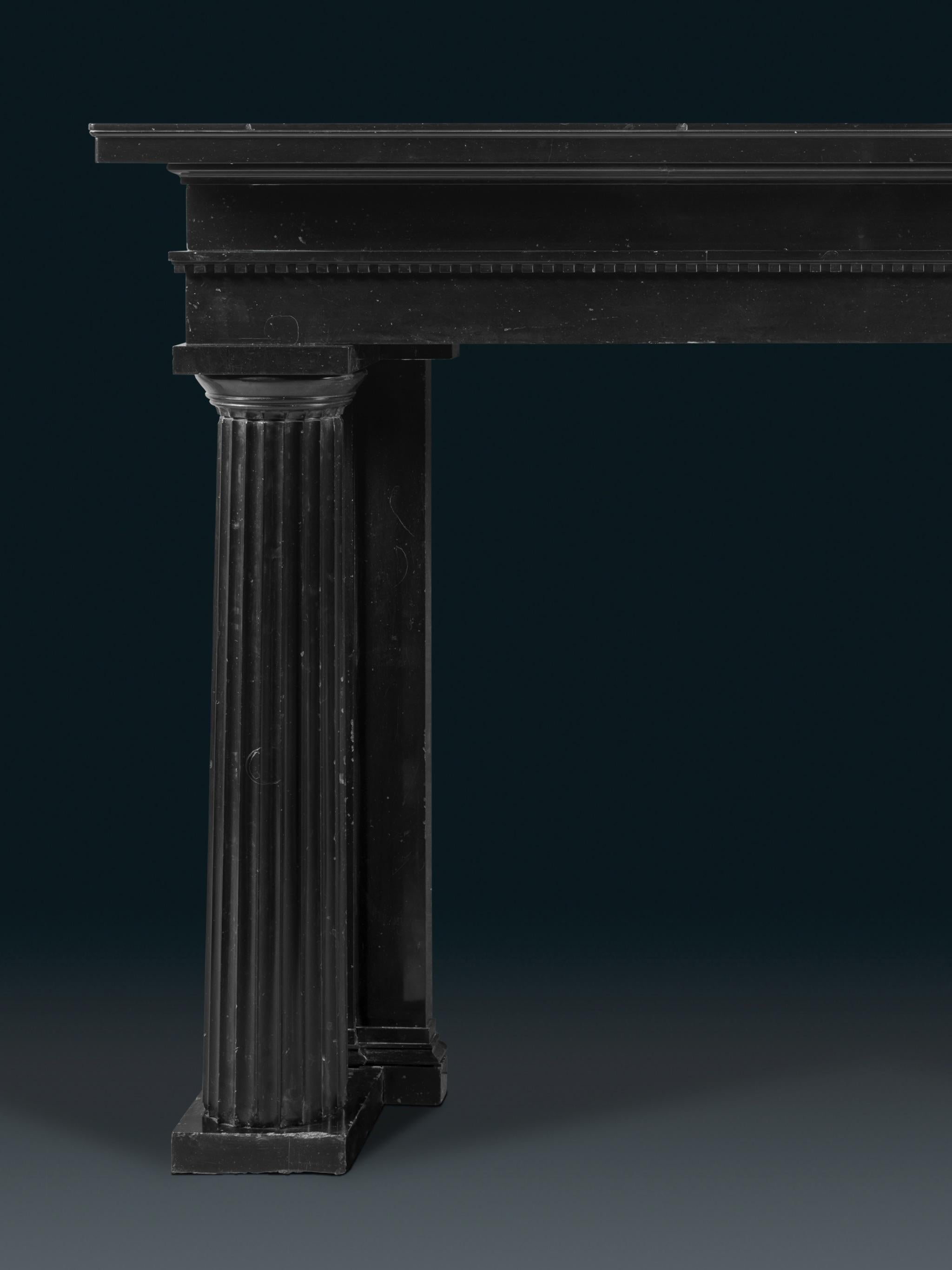 Une cheminée Regency de taille et de prestance, l'ensemble sculpté dans du marbre noir belge, avec des colonnes doriques cannelées en guise de jambages. Ces colonnes utilisent l'entase, c'est-à-dire l'application d'une légère courbe convexe pour