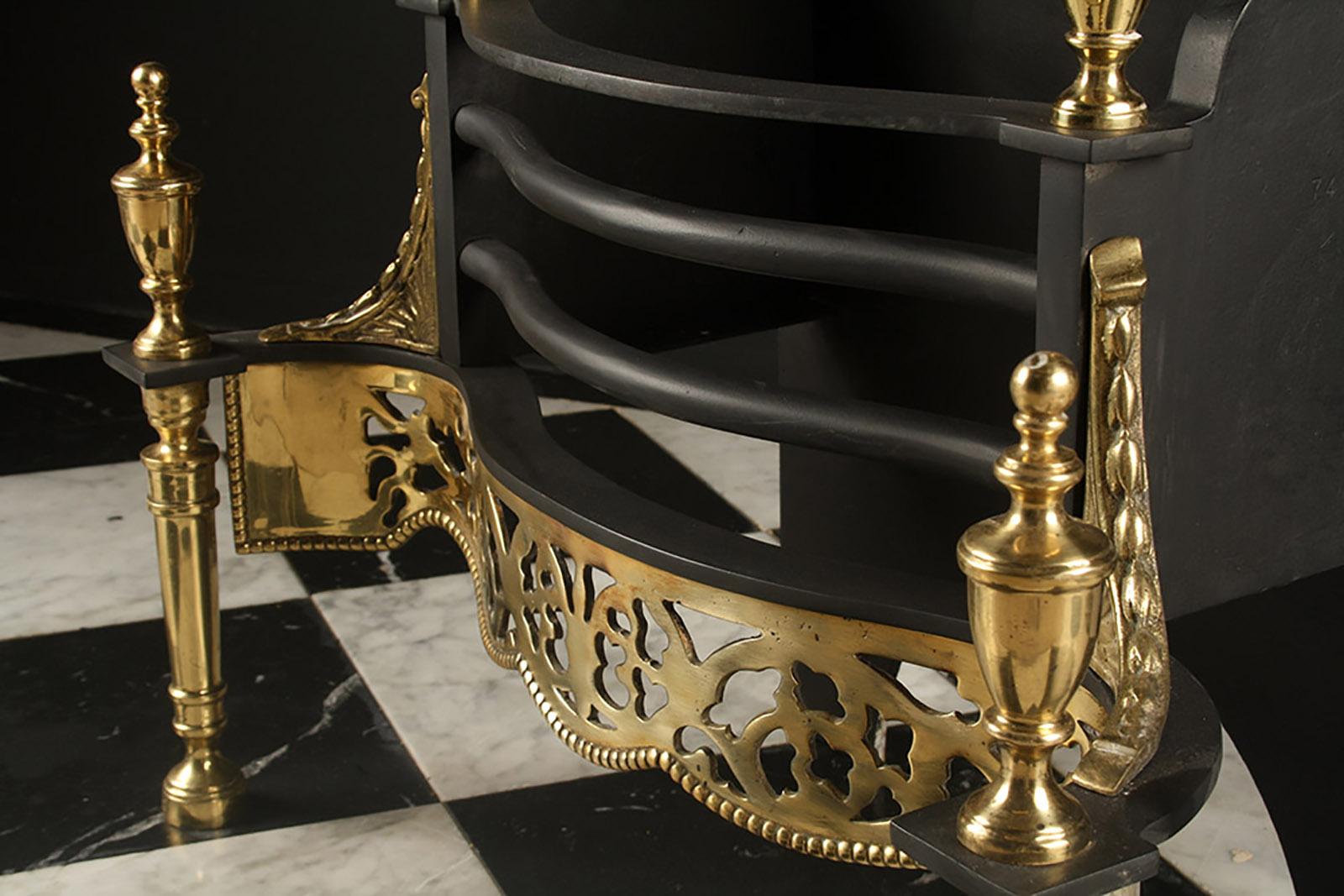 A 20th century George III Regency brass and cast iron serpentine fire grate, with an ornate foliate fret pierced apron and four urn finials, on tapered turned supports, English 20th Century.

Depth: 13 1/2? – 34.2 cm.
External height: 28? – 71