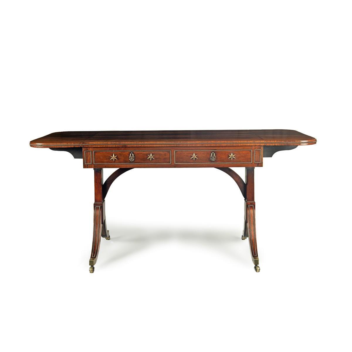 A Regency brass-inlaid rosewood sofa table attributed to Gillows, the rectangular D-end top with two hinged flaps all inlaid with brass beading to the vertical edges, above two frieze drawers with star handles, the square section end supports raised