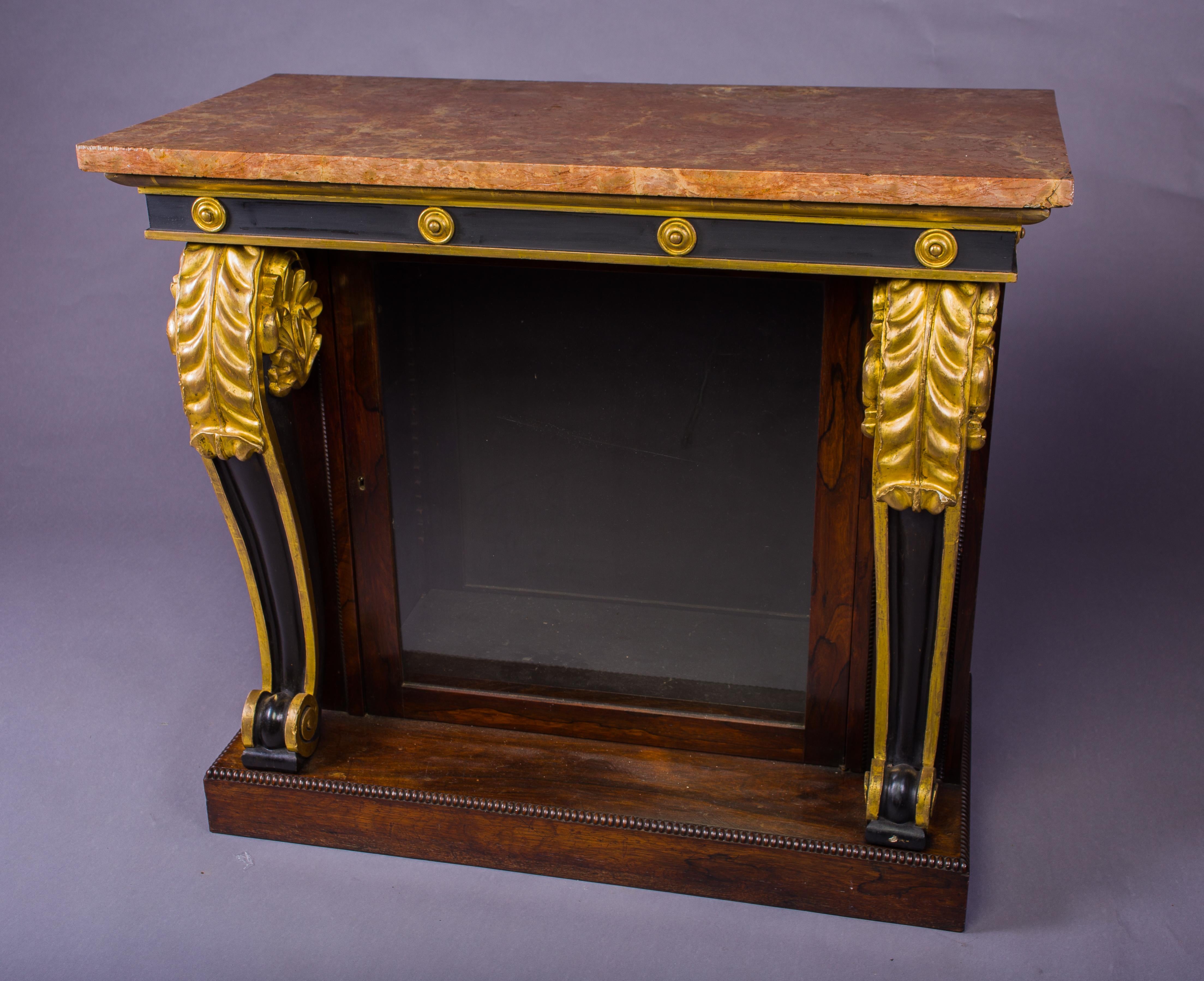 A Robust Regency Rosewood, Gilt-wood and Ebonized Console Cabinet
The original Marseilles pink rectangular marble top, above a gilt-wood moulded and ebonized frieze mounted with roundels, flanked by bold Icanthus carved gilt-wood legs, with a single