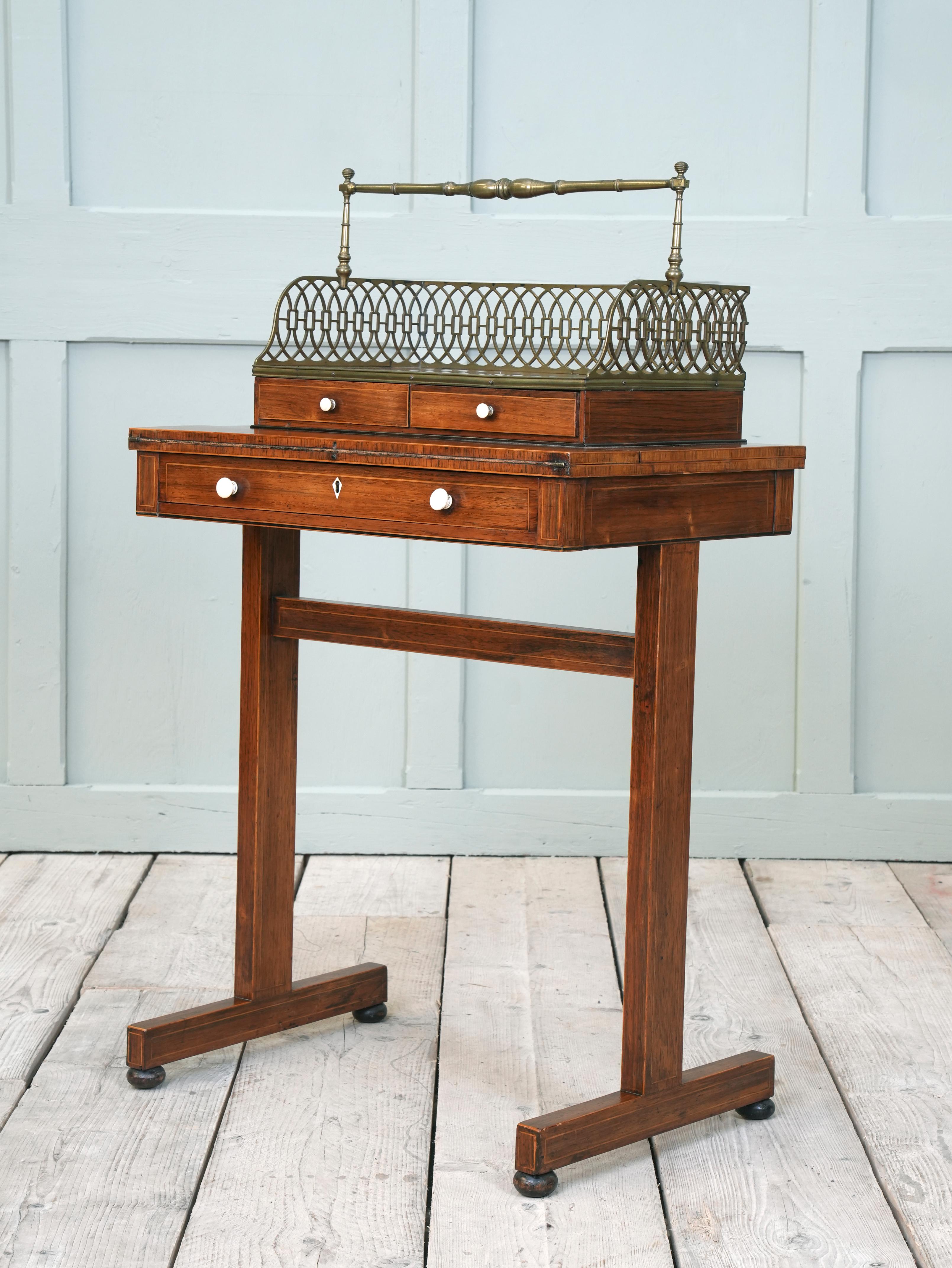 The rosewood ladies writing table raised on a trestle base, folding writing surface with leather insert above a single drawer, the book carrier (Cheveret) with twin drawers and a pierced brass gallery below the turned brass carrying handle, the