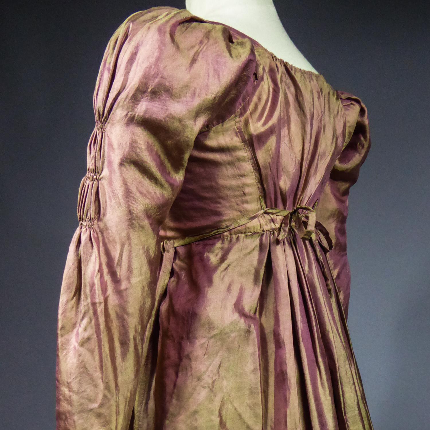 Circa 1810
France

Elegant day dress in silk serge from the First Empire. Very fluid silk with pink chain and olive green weave. Cut with pinned apron on the bodice and integrated corselet in white cotton with eyelets for lacing inside. Cut of the V