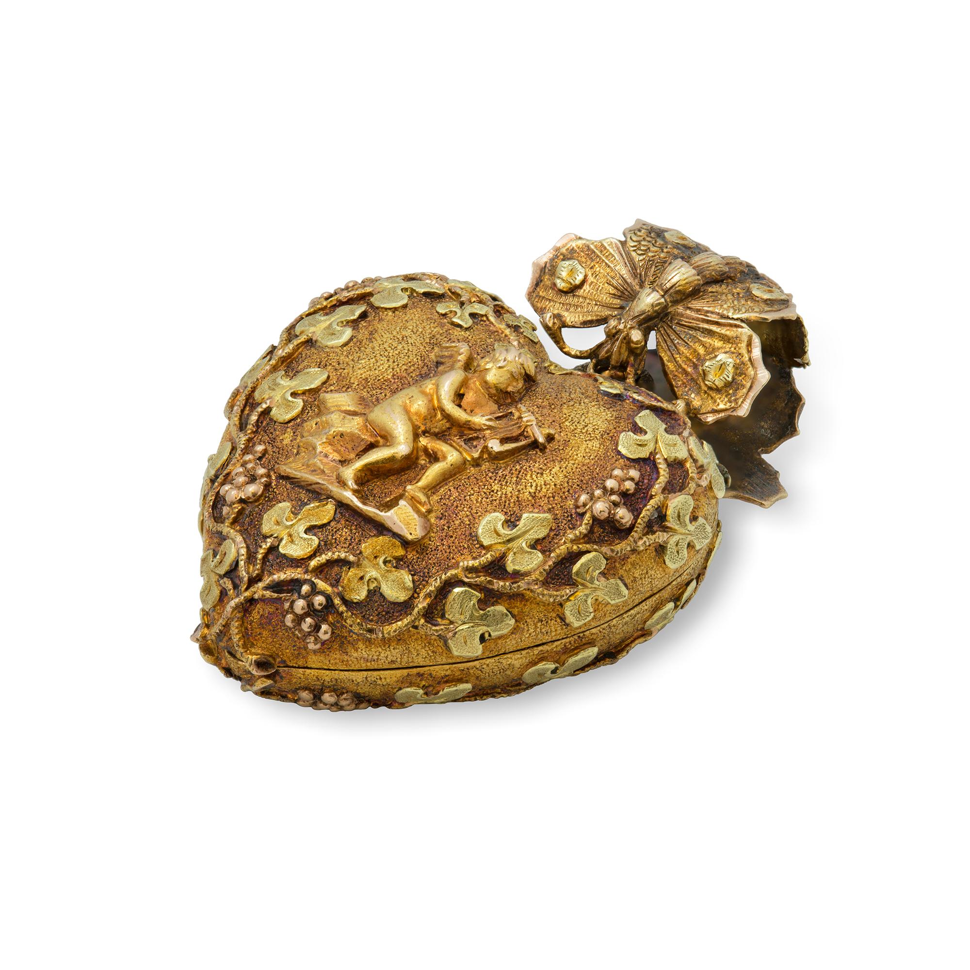 A Regency gold heart locket pendant, at one side depicting a Cupid playing a harp, surrounded by fruiting vines and shamrocks, on the other bearing the word “amitie” meaning friendship, with a locket compartment containing hair, pendant suspending