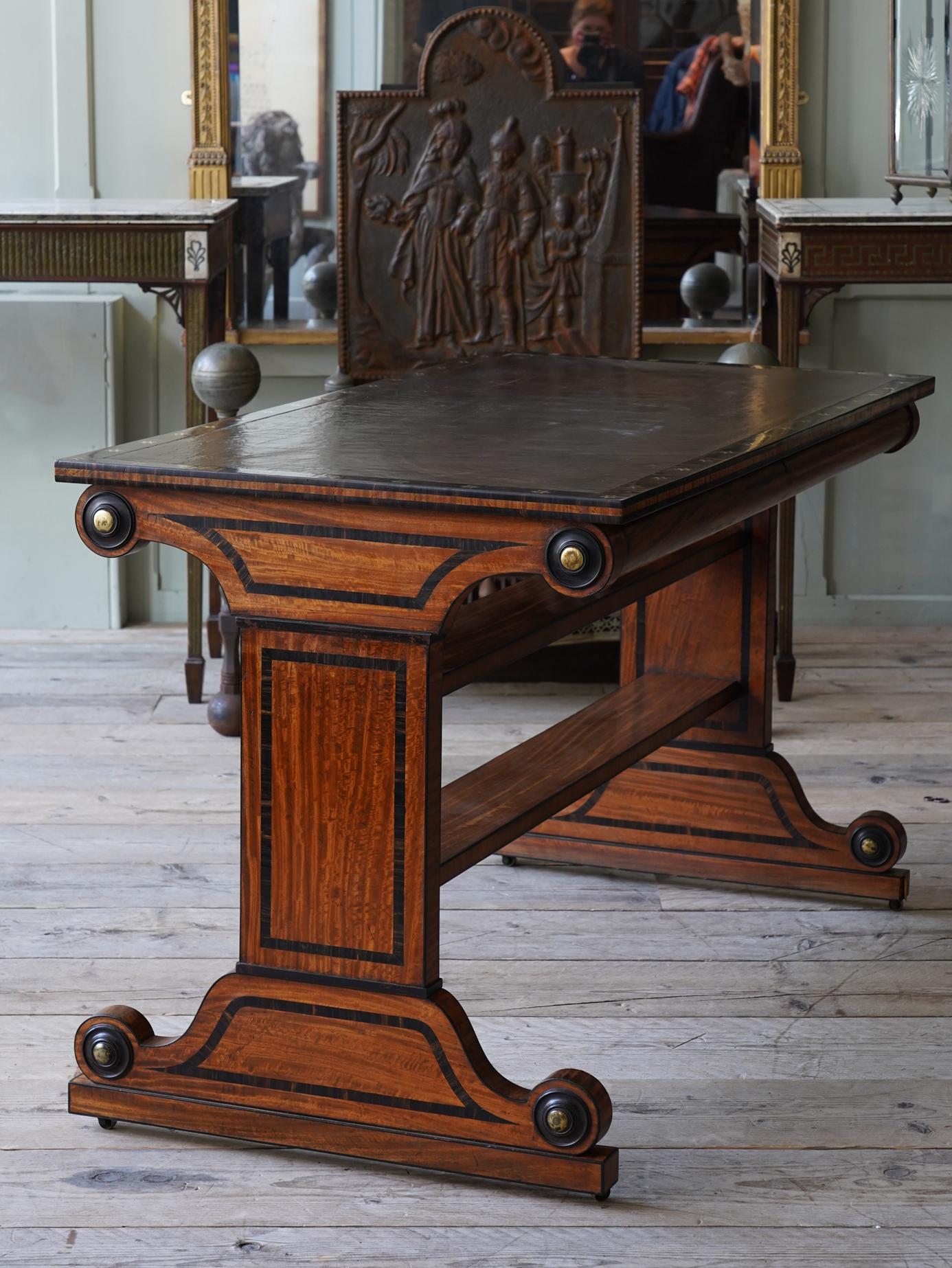 A Regency satinwood and macasar ebony single drawer library table by George Oakley (1773-1840), in the manner of Thomas Hope.

The trestle end supports having brass bosses to each end all with ebony surrounds and are raised on there original brass