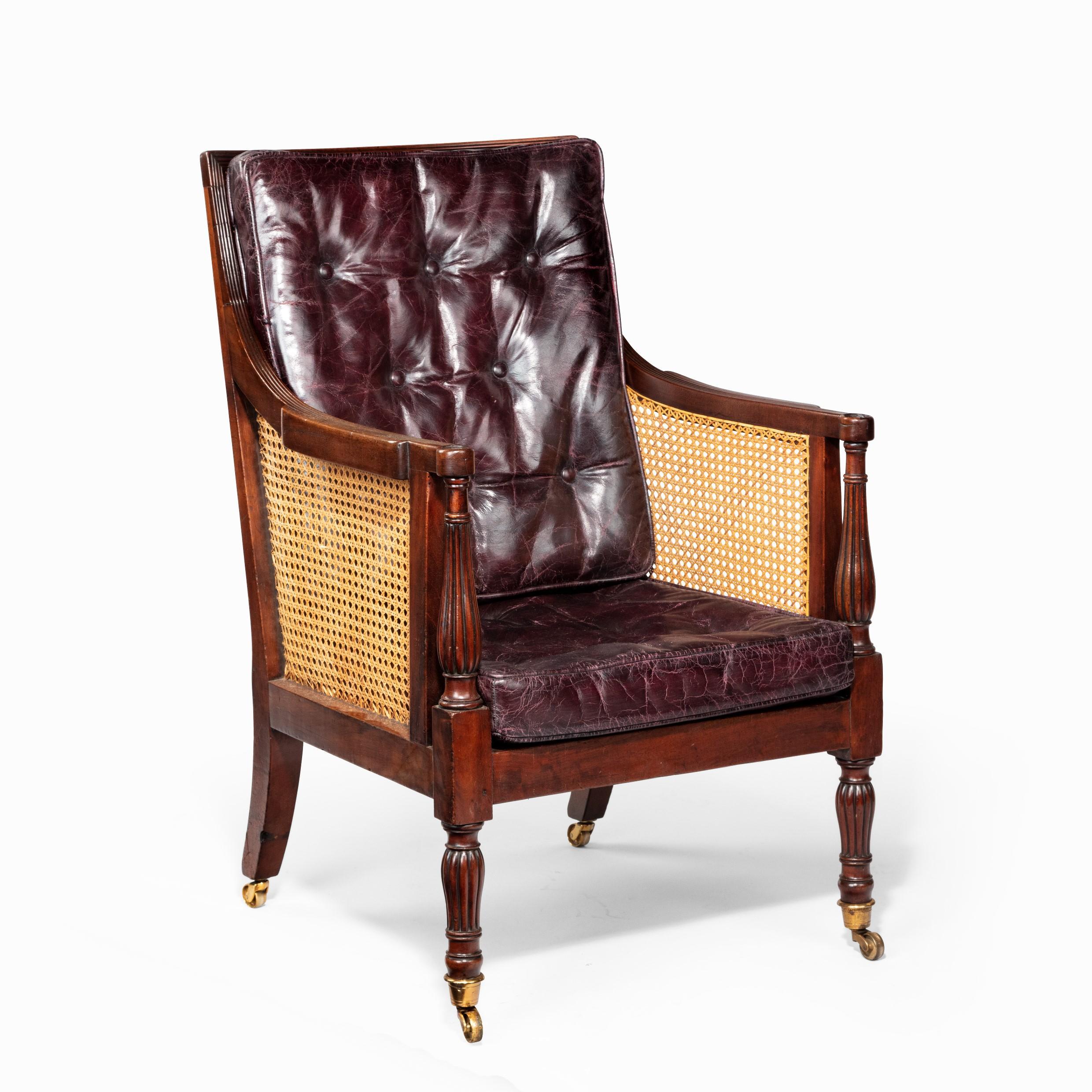 A Regency mahogany bergère chair, with a detachable drinks tray. Rectangular back and seat, the square section arms and seat rails raised on turned baluster front legs and out-swept back legs, re-upholstered in distressed buttoned burgundy leather,